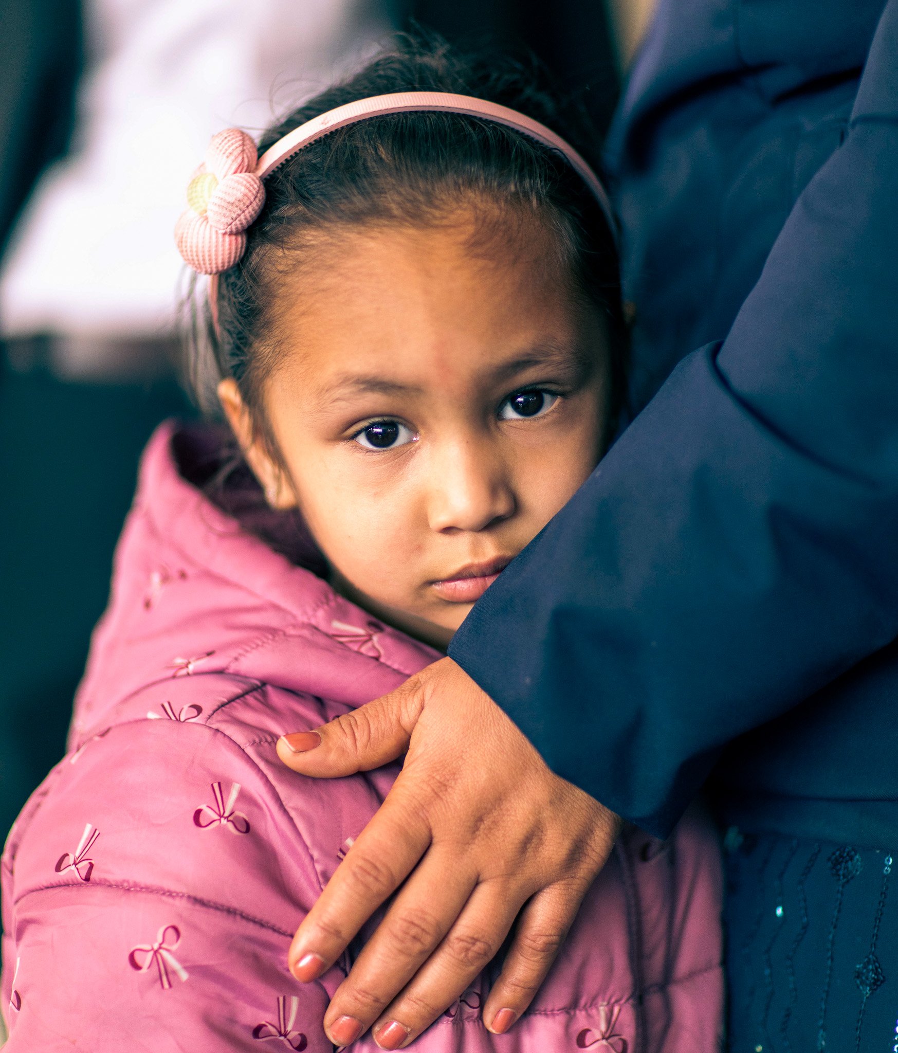 Young girl pink jacket mothers arm around her waiting for eye test. Candid photograph Simon Shattky
