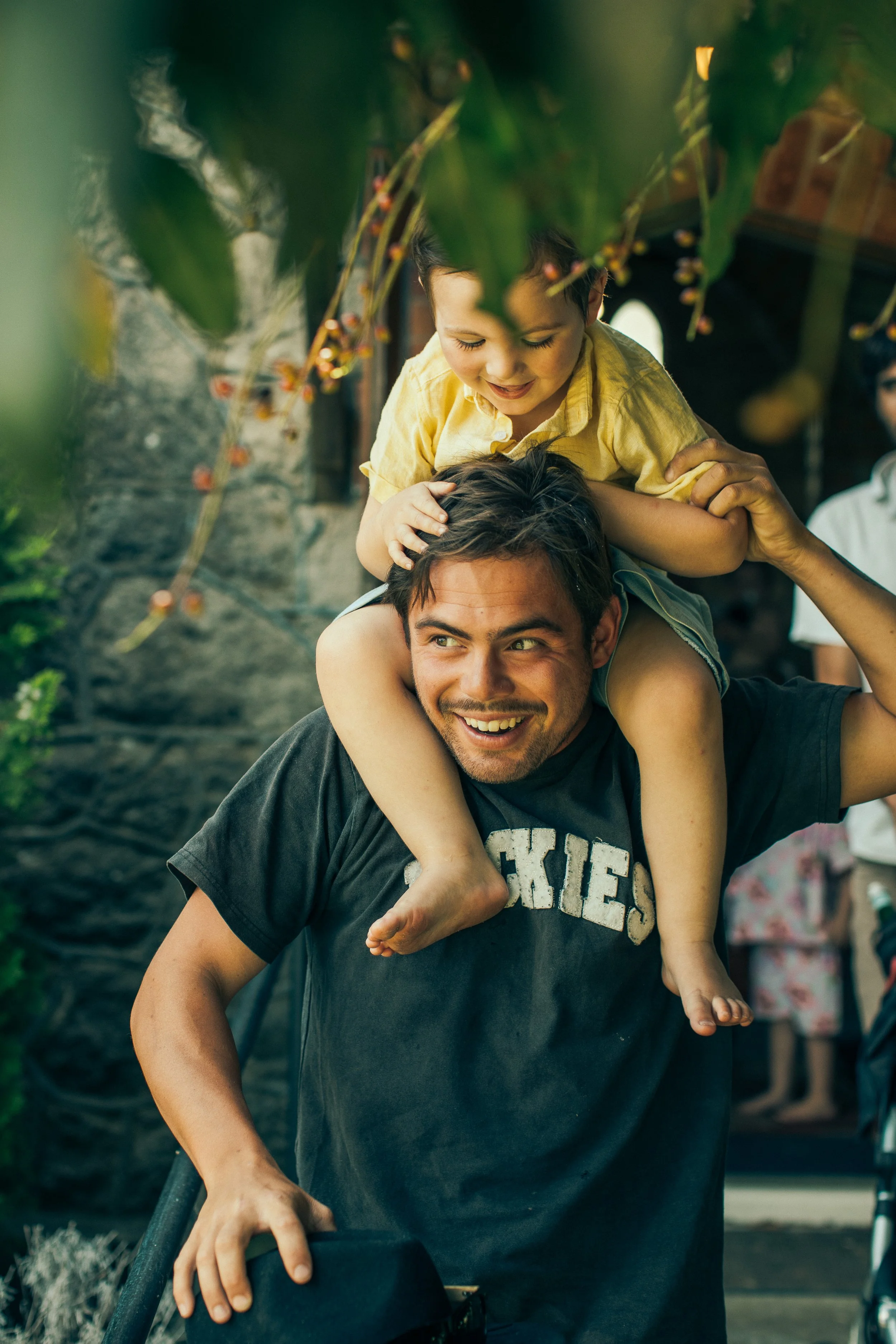 Candid portrait older cousin and child on shoulders at christening celebration laughing Simon Shattky
