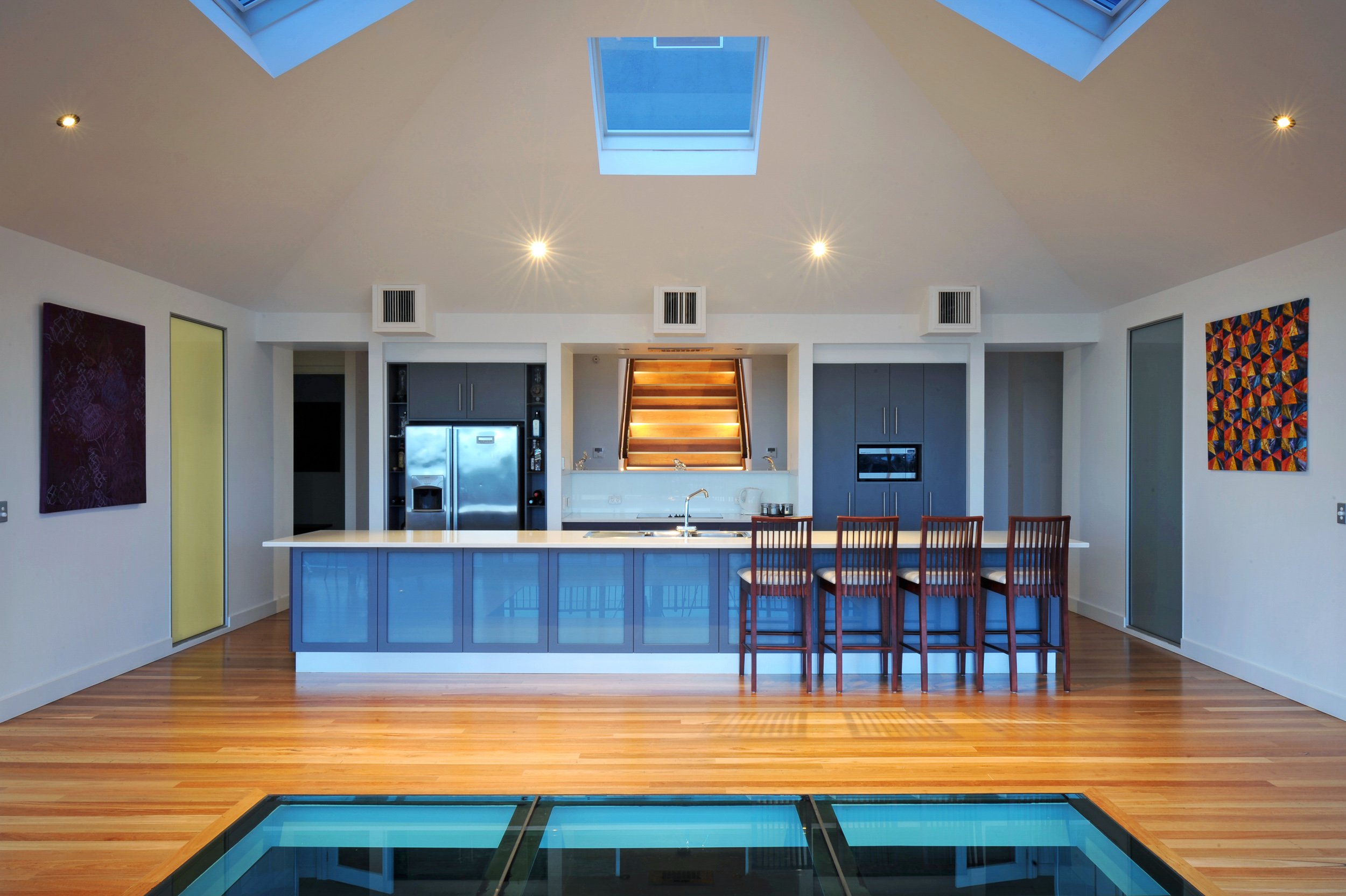 Modern kitchen with blue island, wooden bar stools, gray cabinetry, skylights, and hardwood floors.