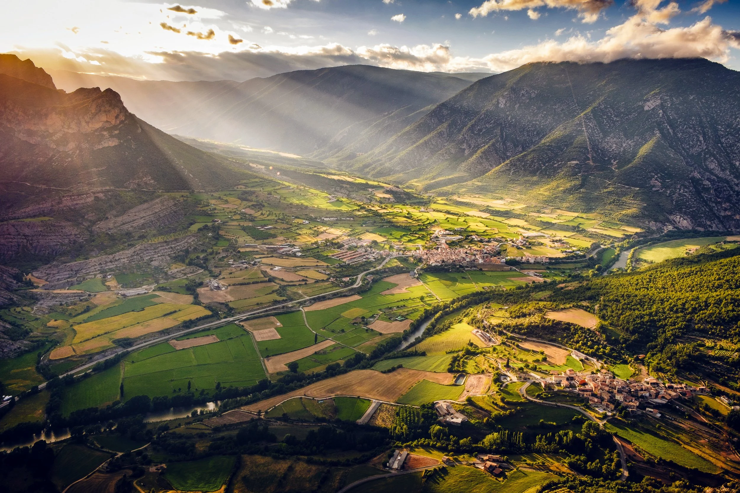 Aerial view of a lush green valley surrounded by mountains with sunlight streaming through clouds.