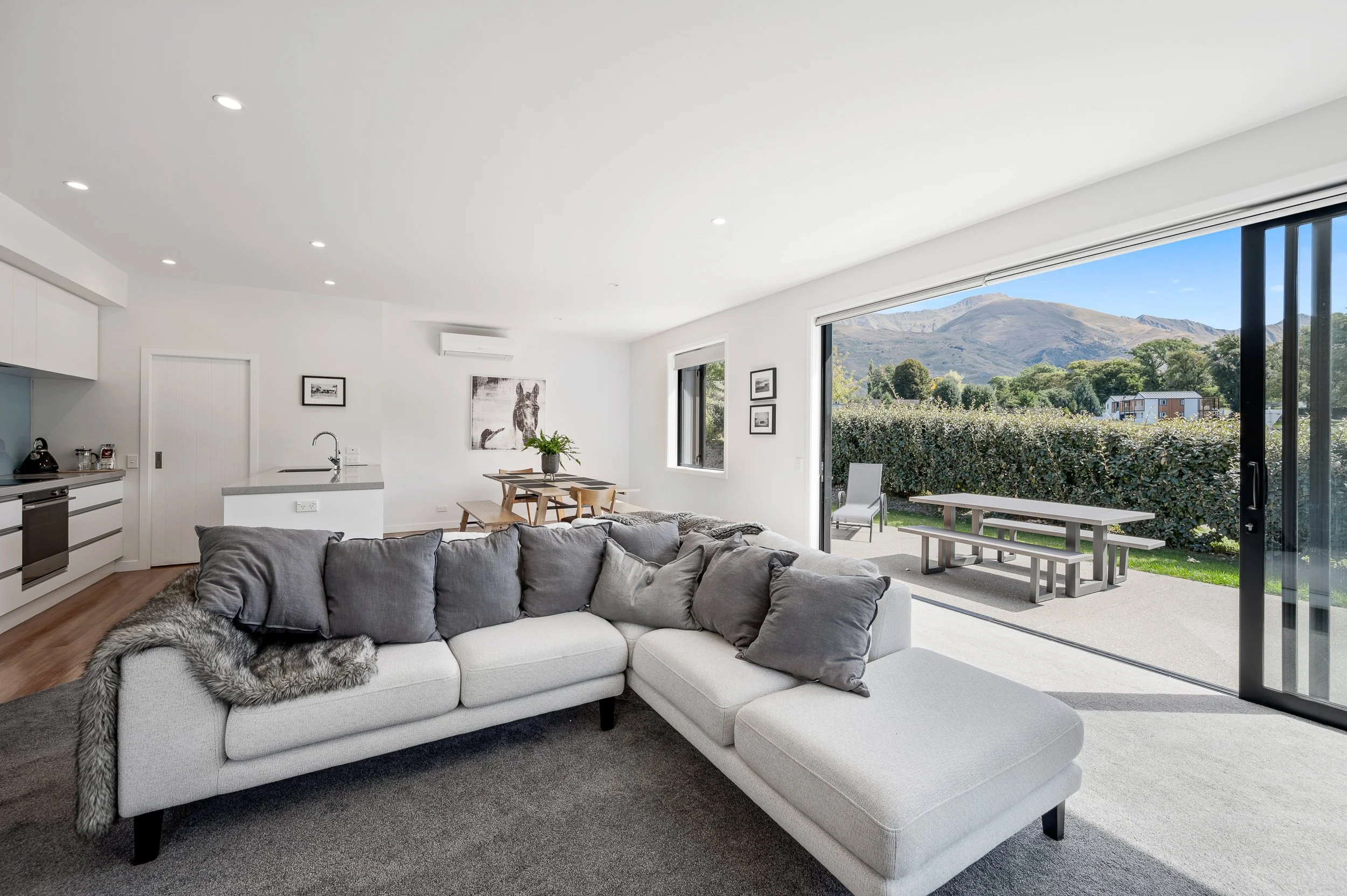 Modern living room with large sliding glass door opening to outdoor patio with mountains in the background.