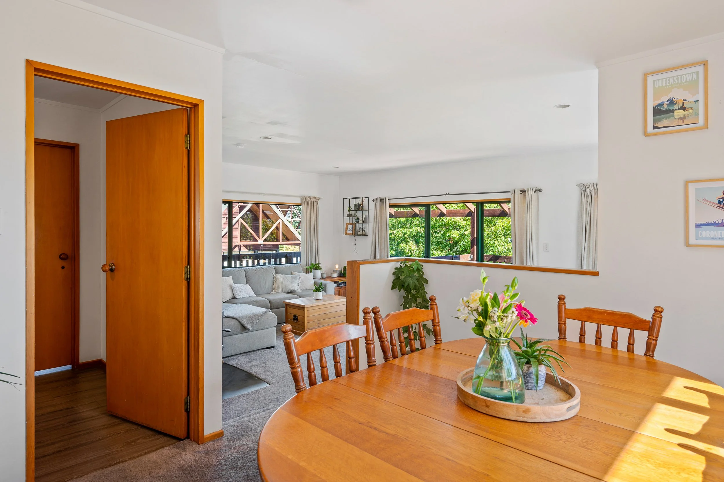 Bright living room and dining area with wooden furniture, large windows, and green outdoor scenery