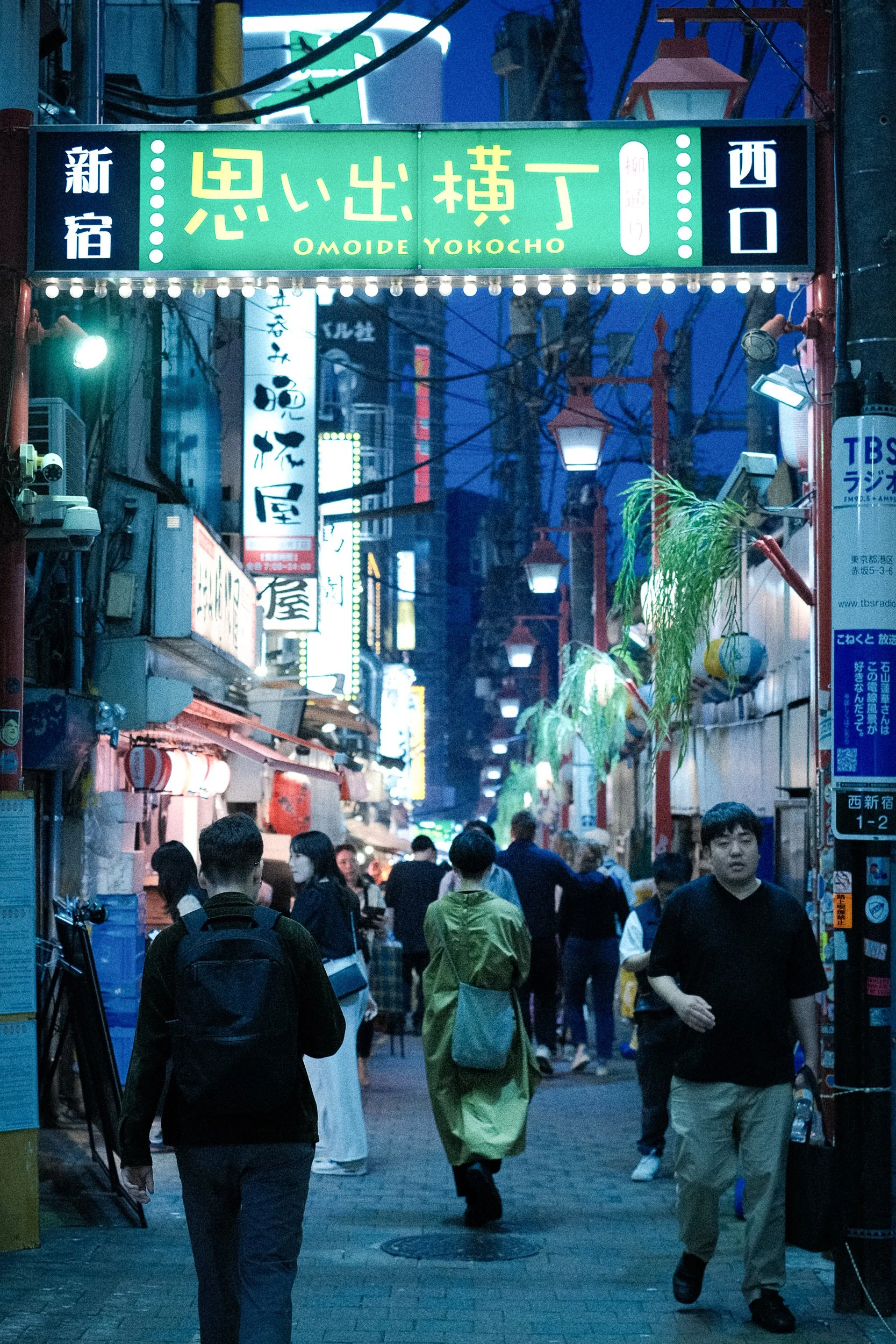 Night scene of a busy street in Tokyo, Japan, filled with pedestrians and illuminated signs in Japanese, with lanterns hanging overhead.