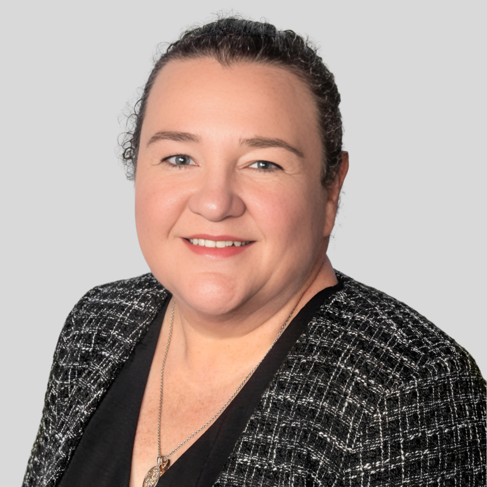 A professional woman smiling, wearing a black top and a black and white checkered blazer, with a necklace, against a light gray background.