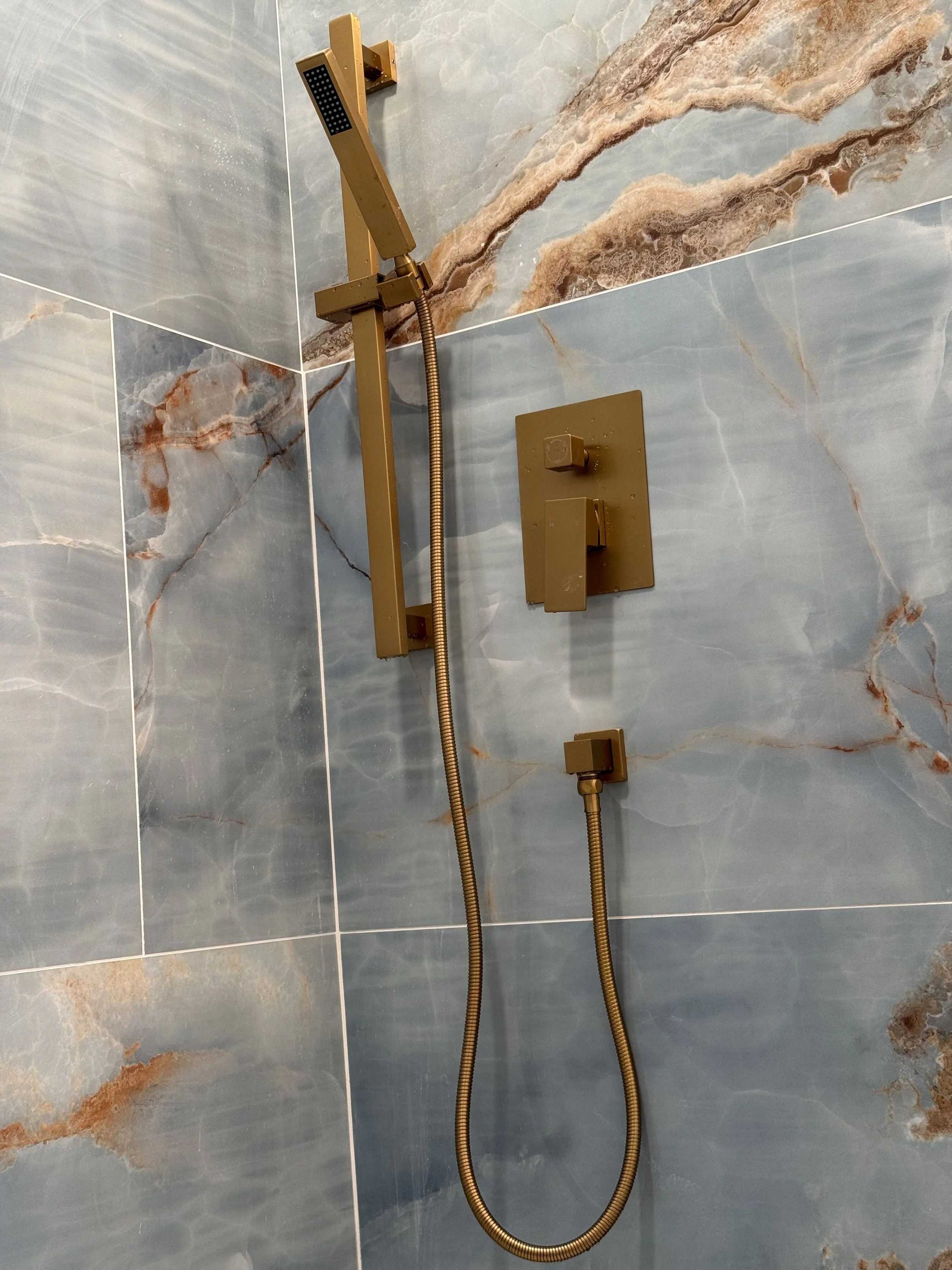 Shower head and handle in a bathroom with blue and brown marbled tiles.