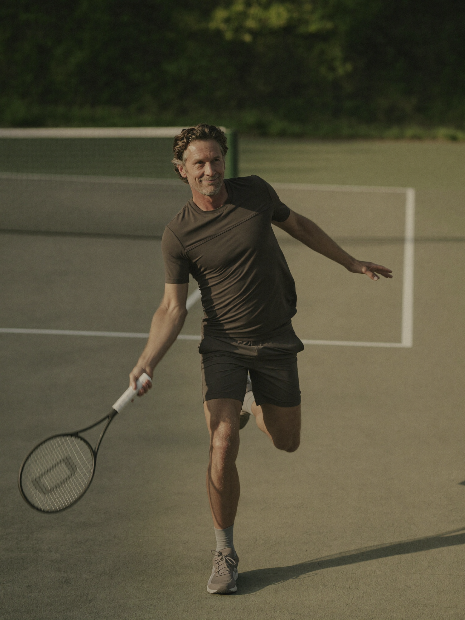 A man with gray hair and a beard playing pickleball on a court at dusk