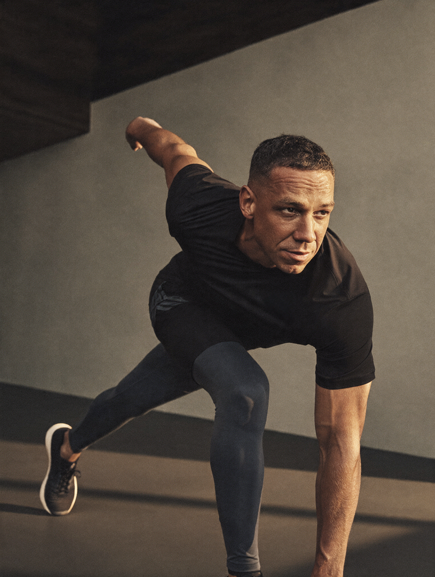 Man doing a workout or exercise in a gym, lunging with one arm extended behind him.