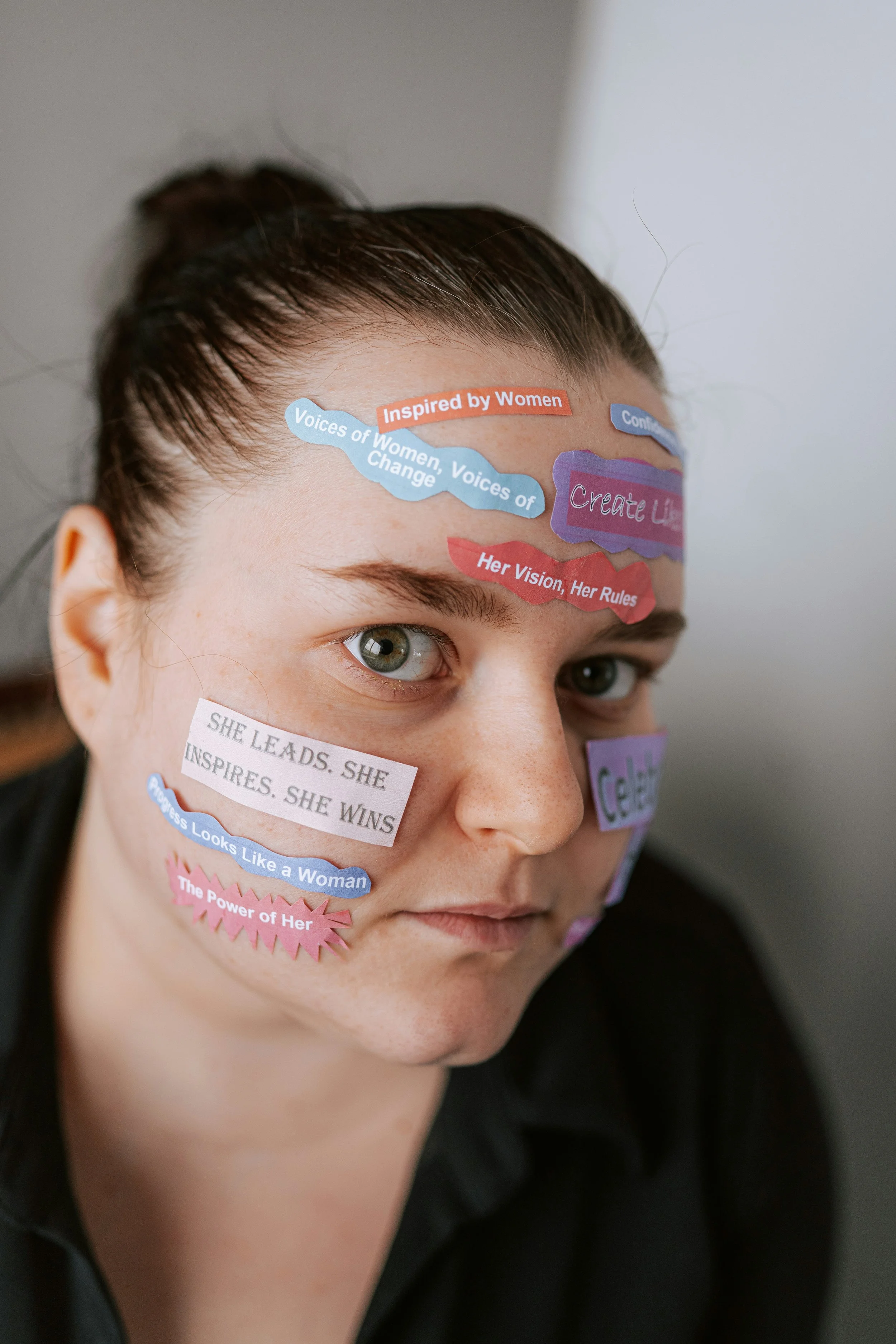 Close-up of a woman with various colorful stickers on her face containing motivational messages about women and empowerment.