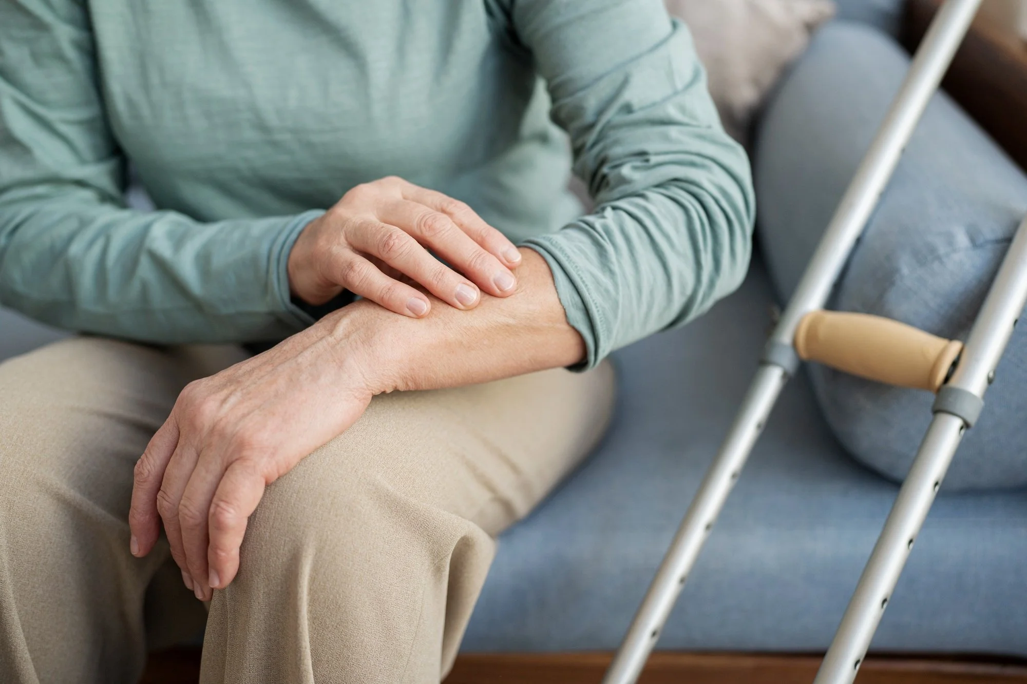 Close-up of an elderly person's hand being gently held by a caregiver, with a walker nearby.