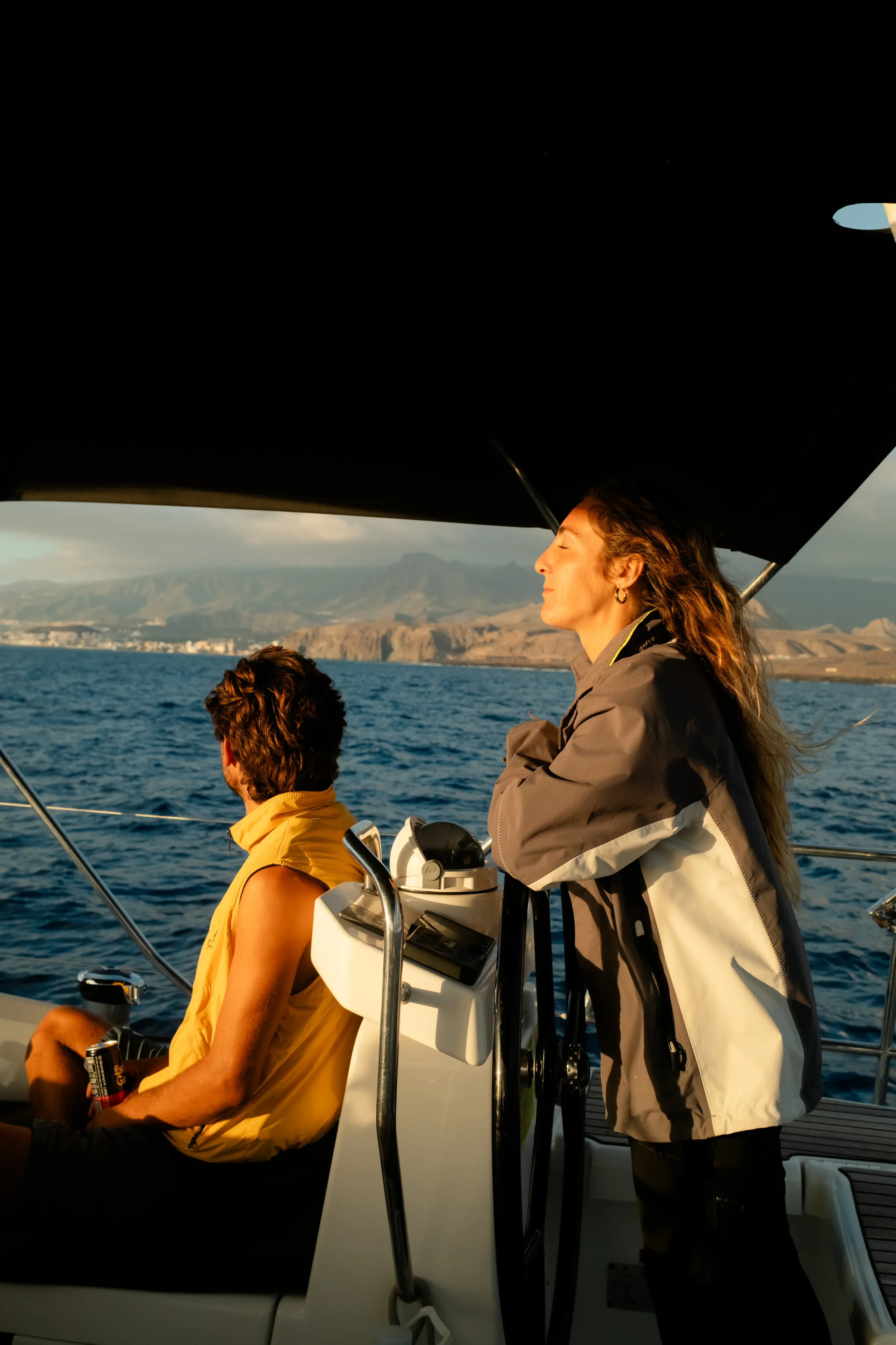 Two people on a boat enjoying a sunny day on the water with mountains in the background.