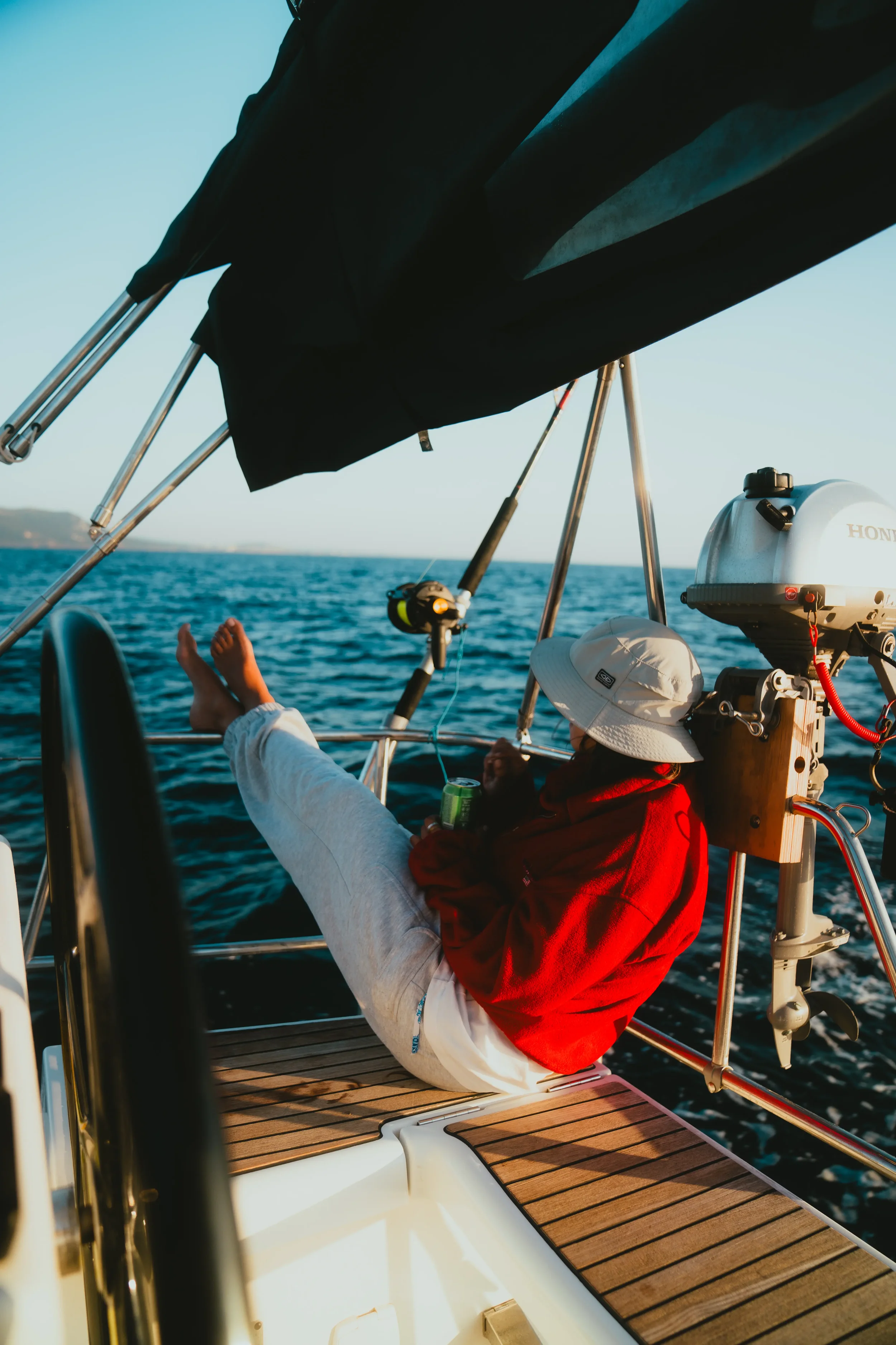 Person relaxing on a boat with their feet up, wearing a white hat and red jacket, surrounded by boating equipment and ocean view.