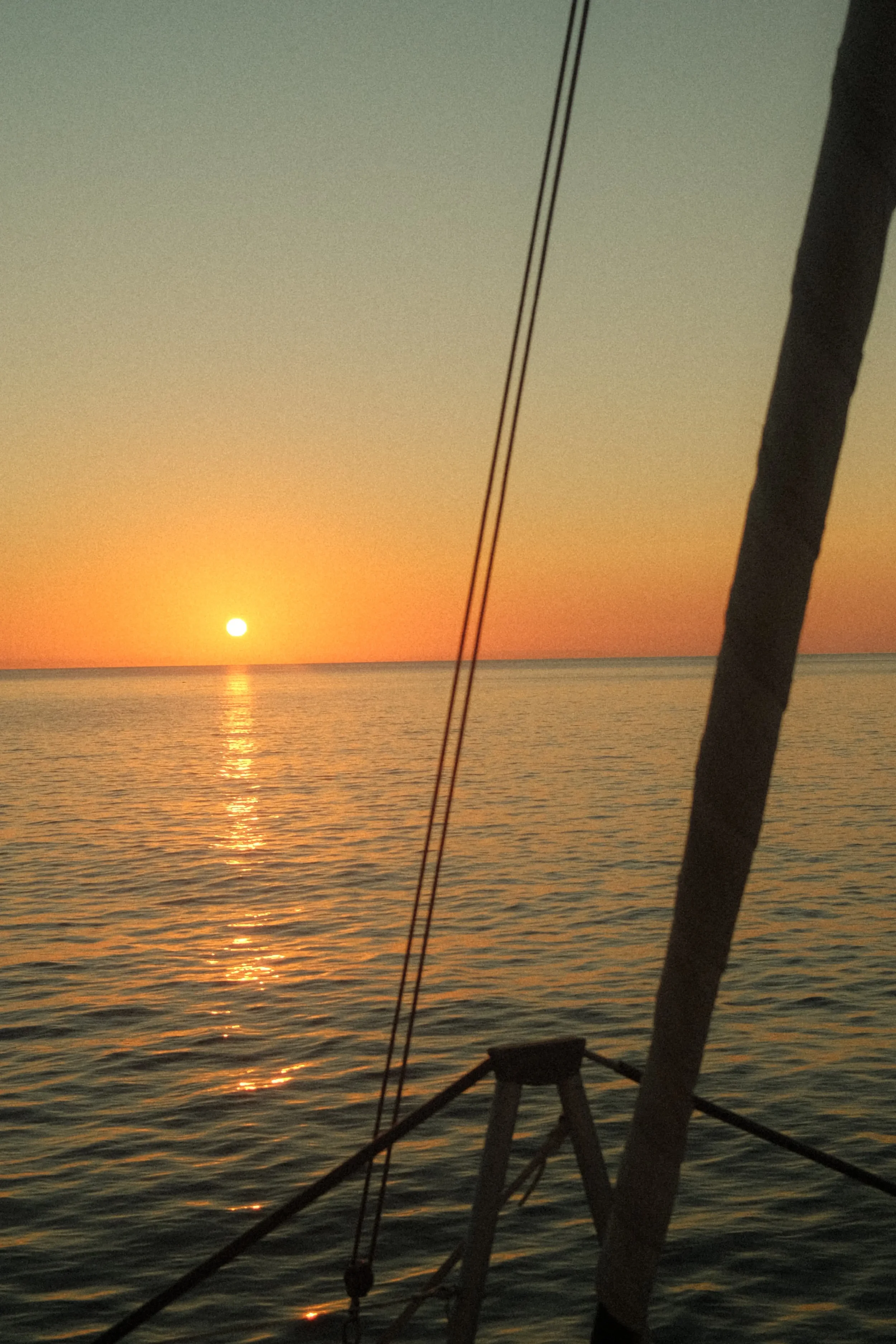 Sun setting over the ocean with silhouettes of boat rigging in the foreground