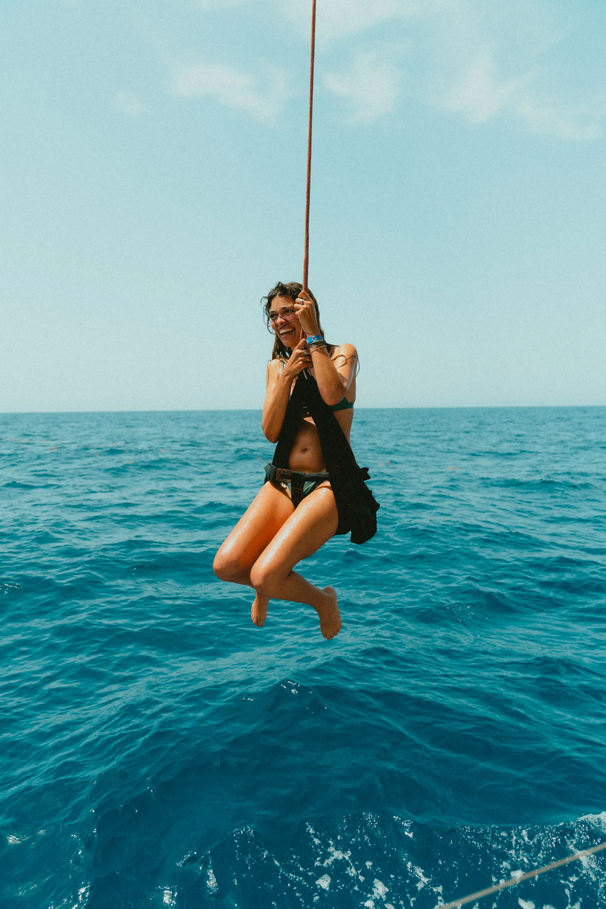 A woman smiling and enjoying a swing over the ocean on a sunny day.