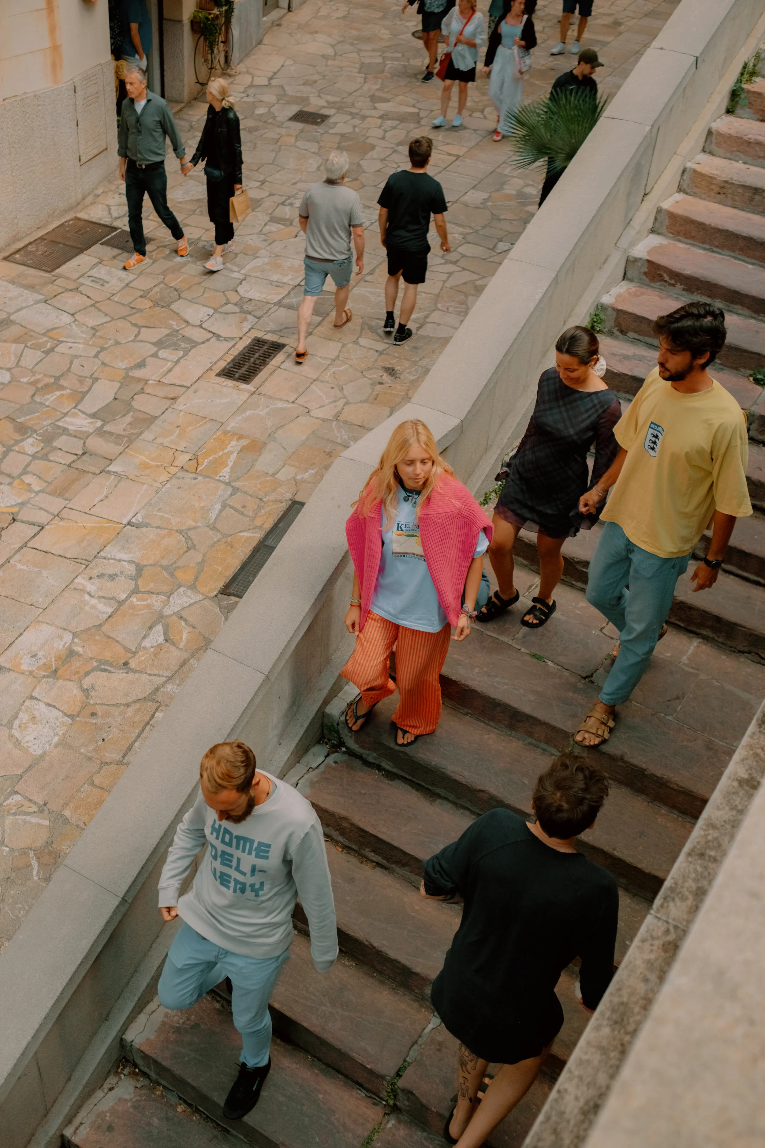 People walking on a cobblestone street near stairs and a wall.