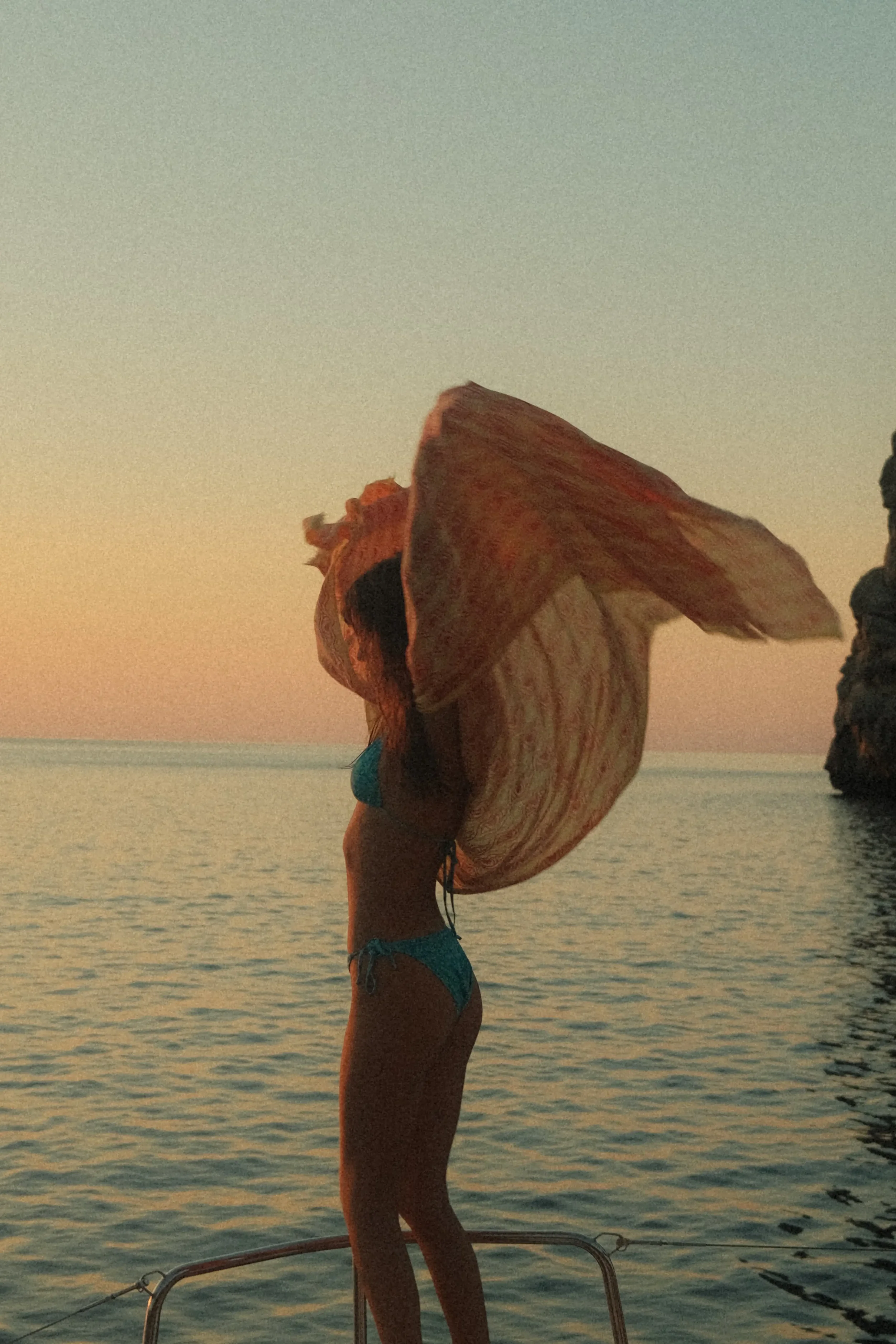 A woman in a bikini on a boat holding a large shell, with water and a sunset sky in the background.