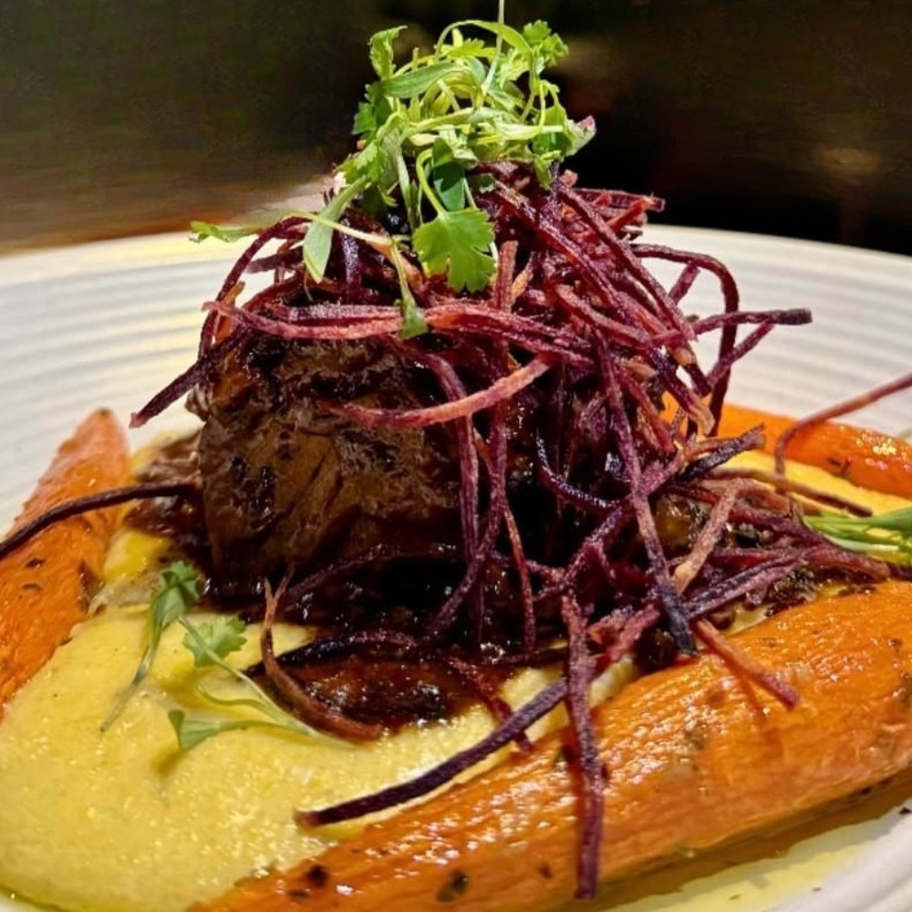 Roasted sweet potato topped with shredded beetroot, fresh cilantro, and sauce, served on a white plate.