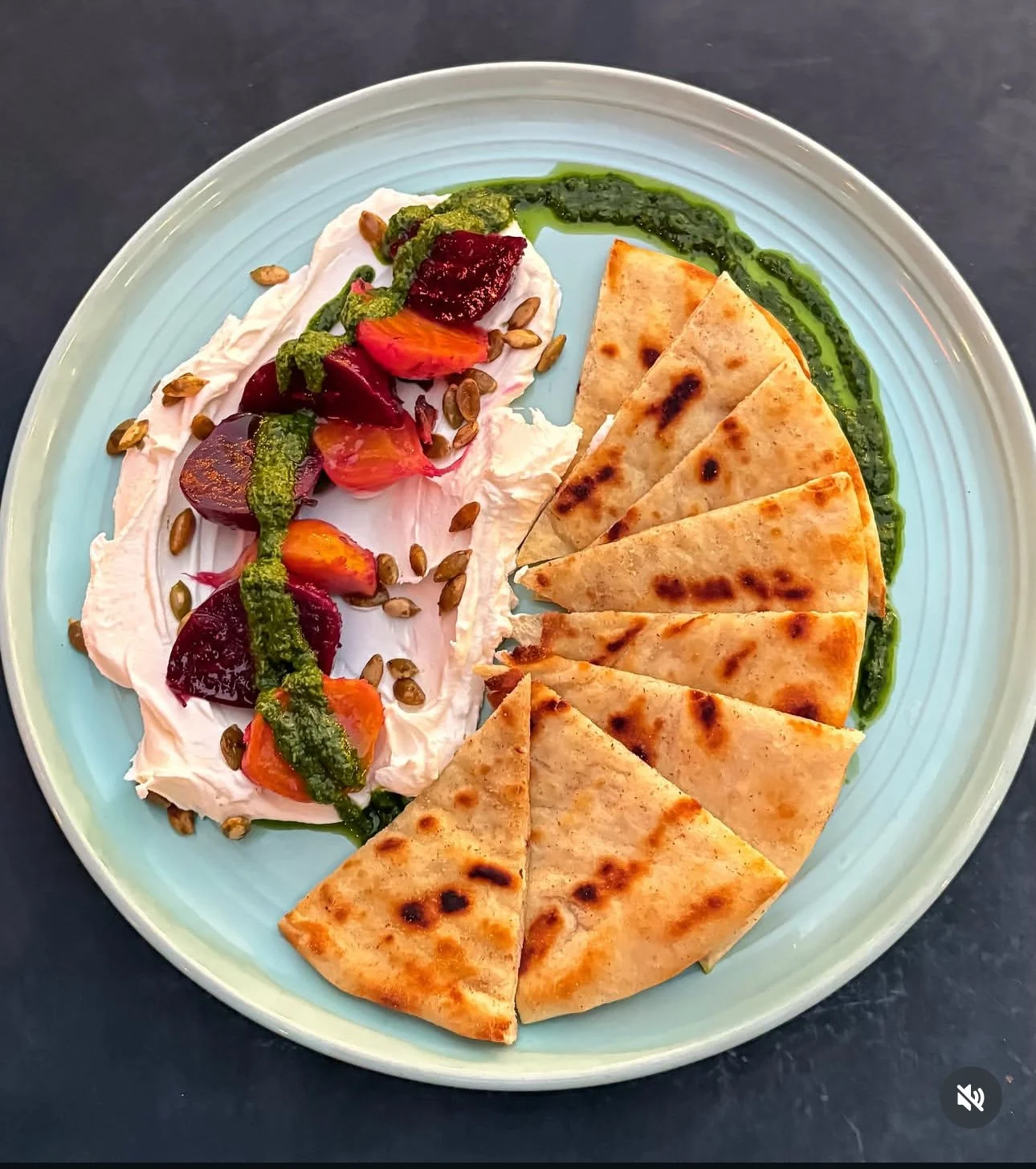 A plate of sliced quesadilla with green sauce, served alongside a creamy spread topped with roasted vegetables, seeds, and green sauce.