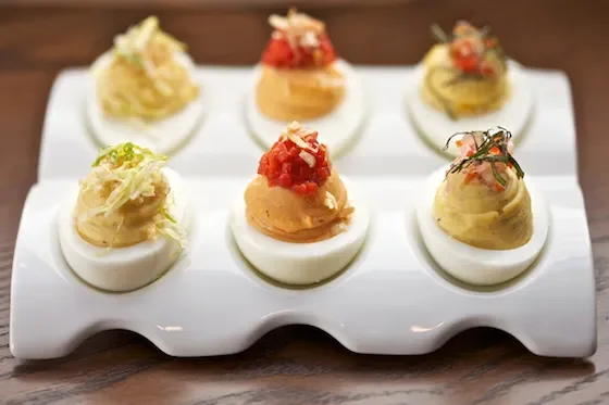 Six deviled eggs topped with various garnishes on a white platter.
