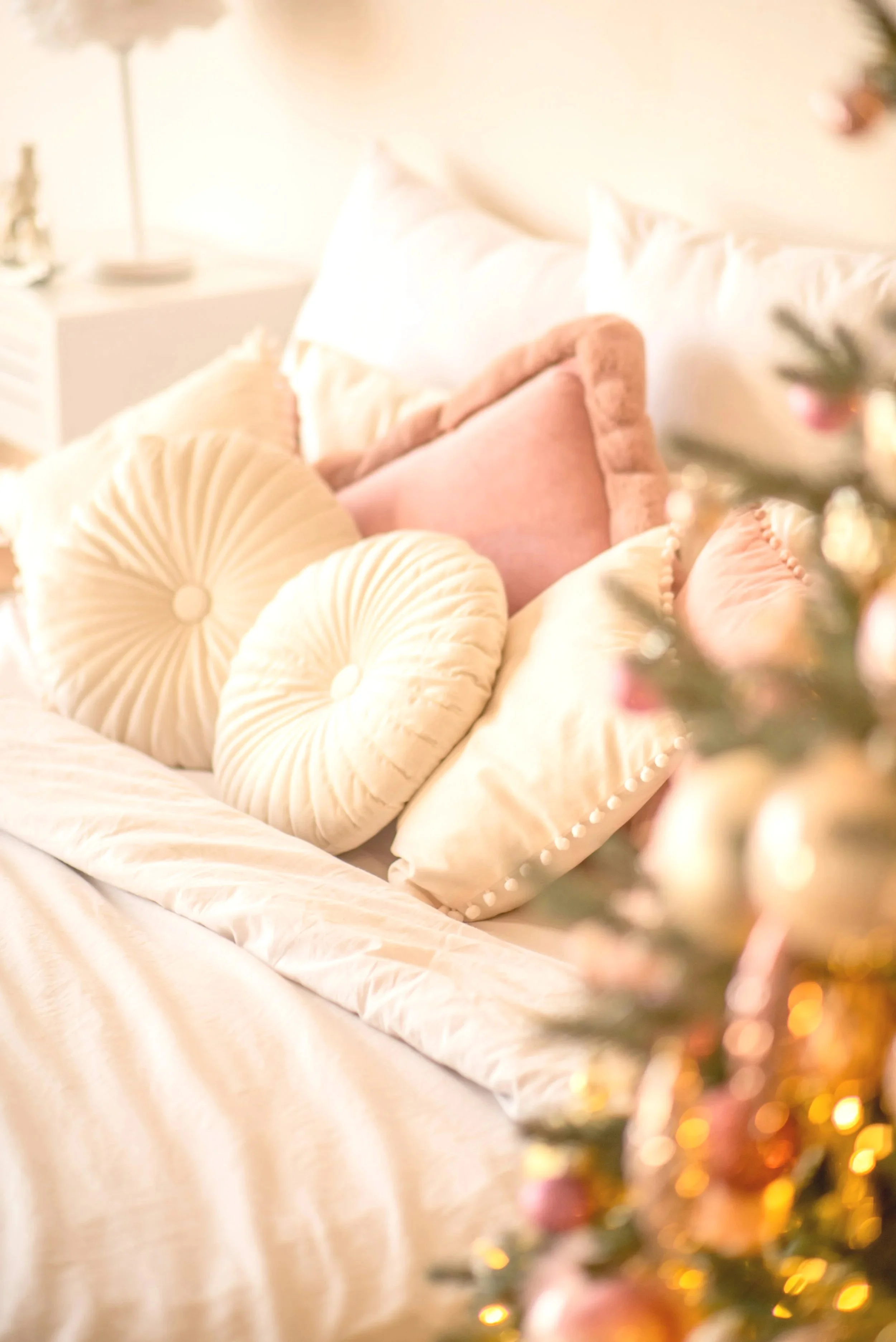 A bed with cream and pink decorative pillows and a festive Christmas tree in the foreground.