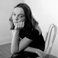 Black and white photo of a young woman with chin resting on her hand, sitting on a chair.