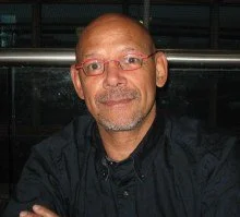 A man with glasses and a goatee, wearing a black shirt, smiling at the camera.