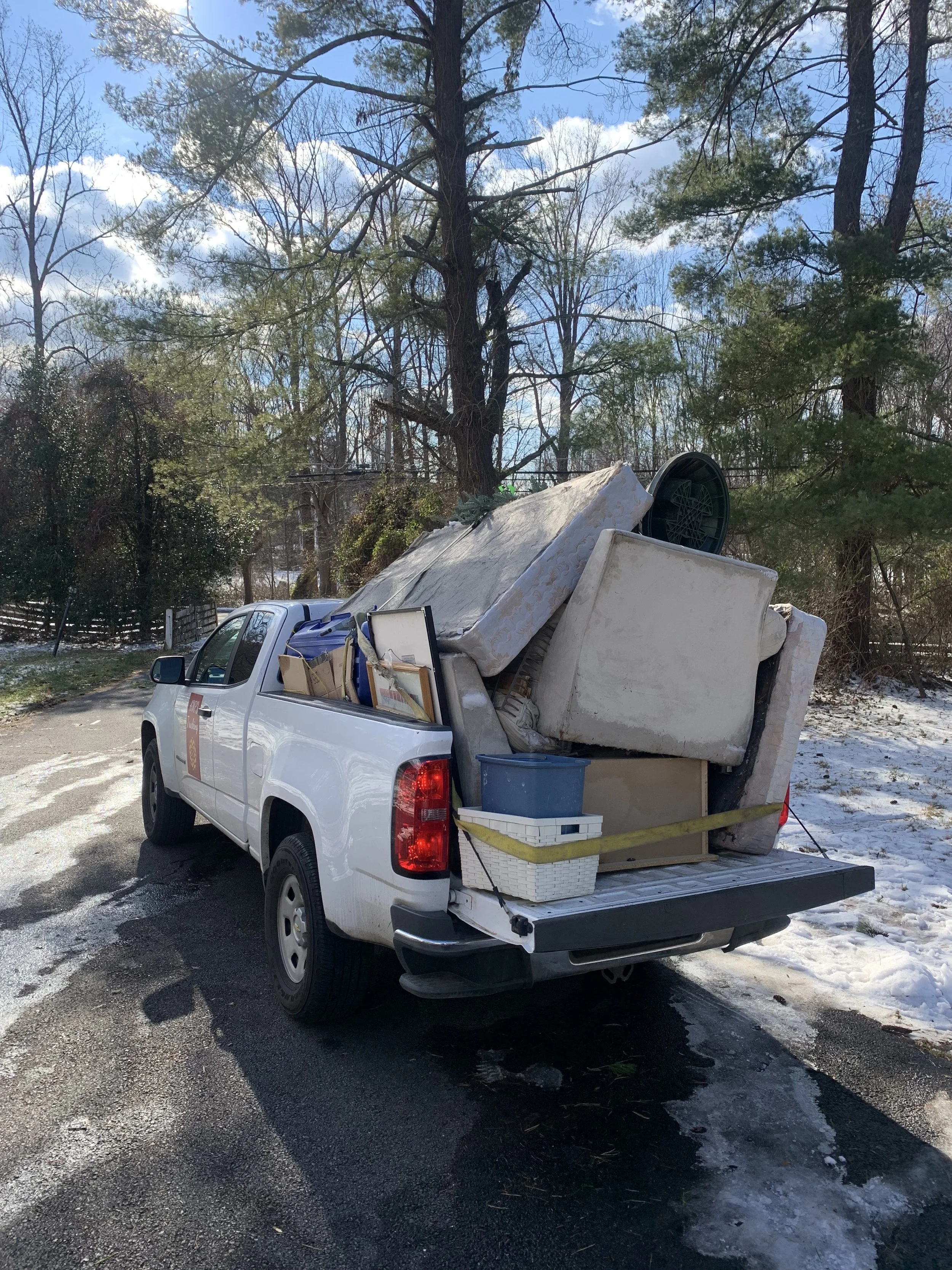 Pickup truck filled with old furniture and household items, parked on a driveway with trees in the background.
