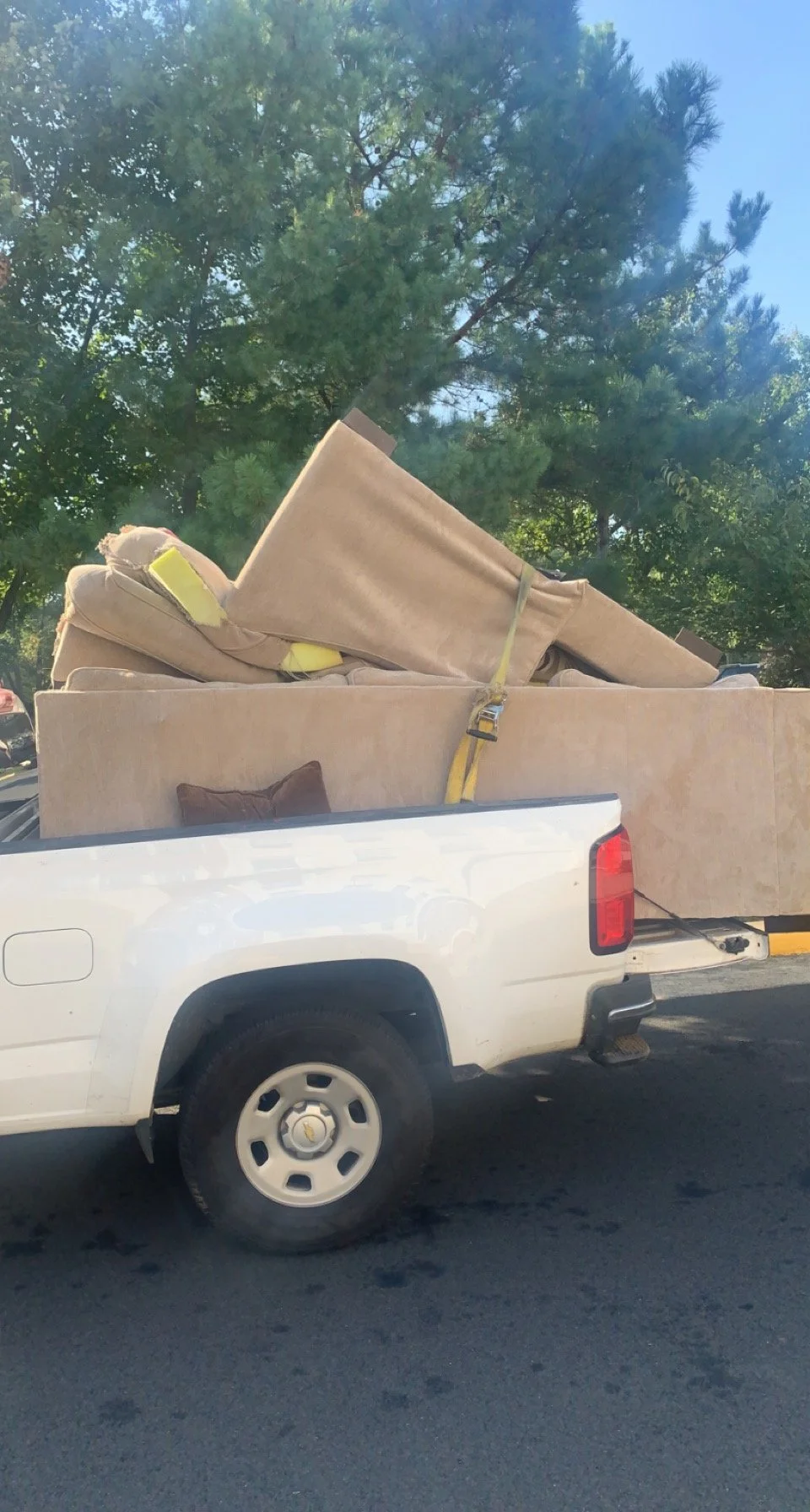 Pickup truck loaded with furniture, including a couch and mattresses, parked outdoors with trees in the background.