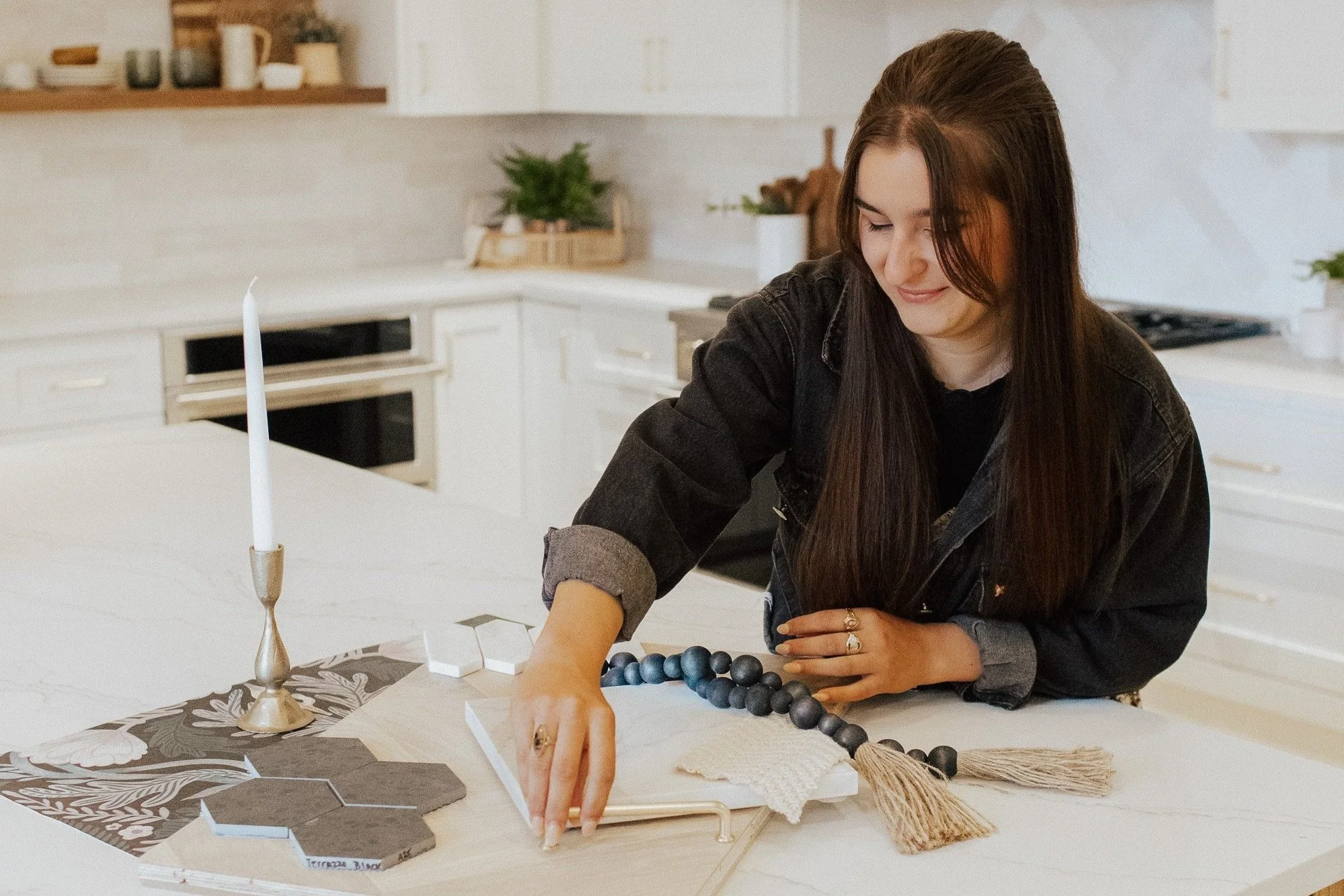 Woman arranging decorative items like beads and fabric on a table in a bright, modern kitchen.