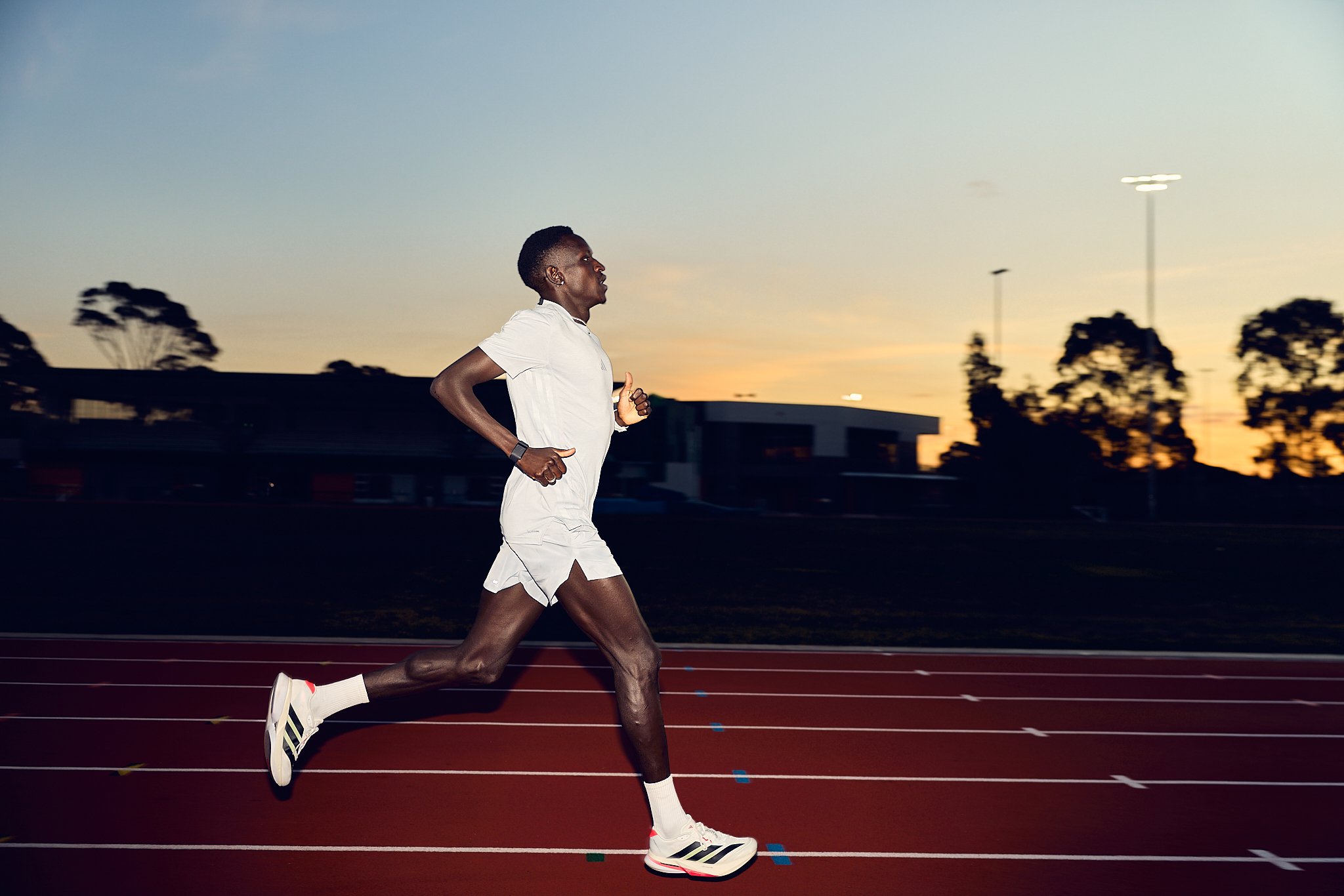 A male runner in white athletic clothing running on a track at sunset