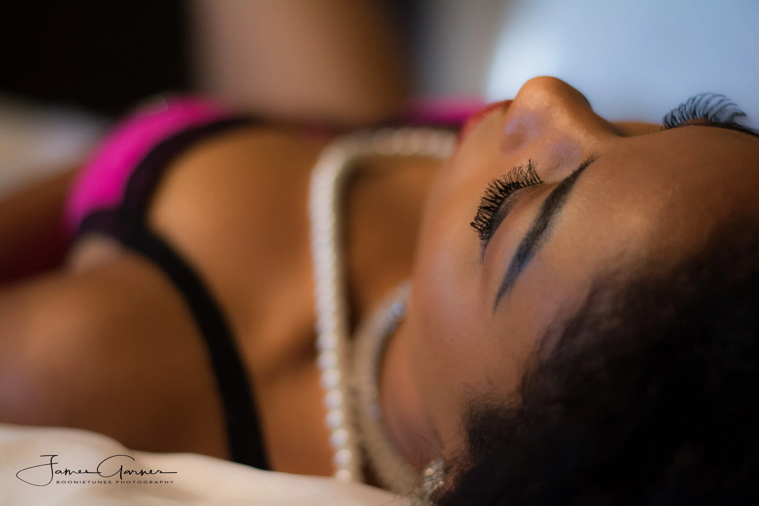 Close-up of a woman's face showing her closed eye with long eyelashes, makeup, and jewelry, with a blurred background.