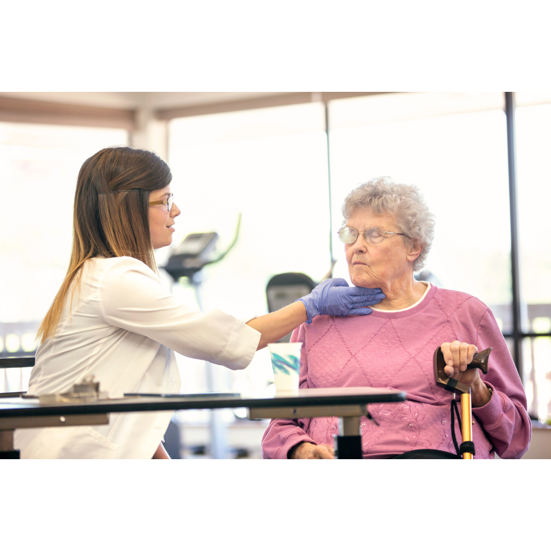 A healthcare worker checks an elder woman's throat while she swallows liquids seated in a wheelchair, in a bright care facility.