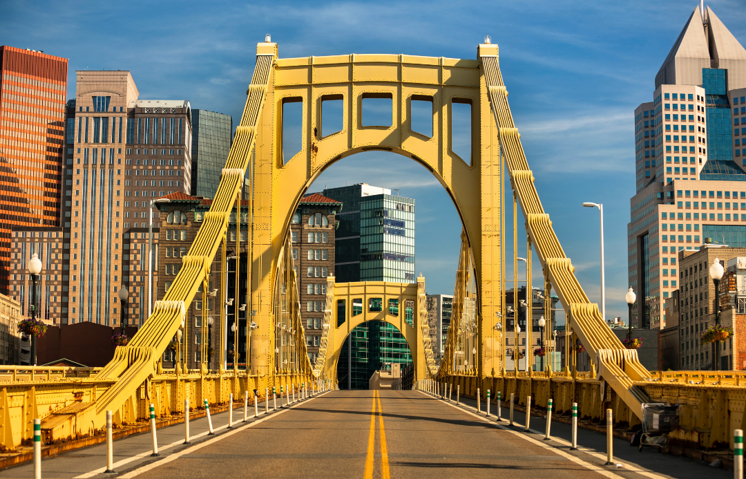 View of a yellow suspension bridge in a city with modern high-rise buildings in the background.