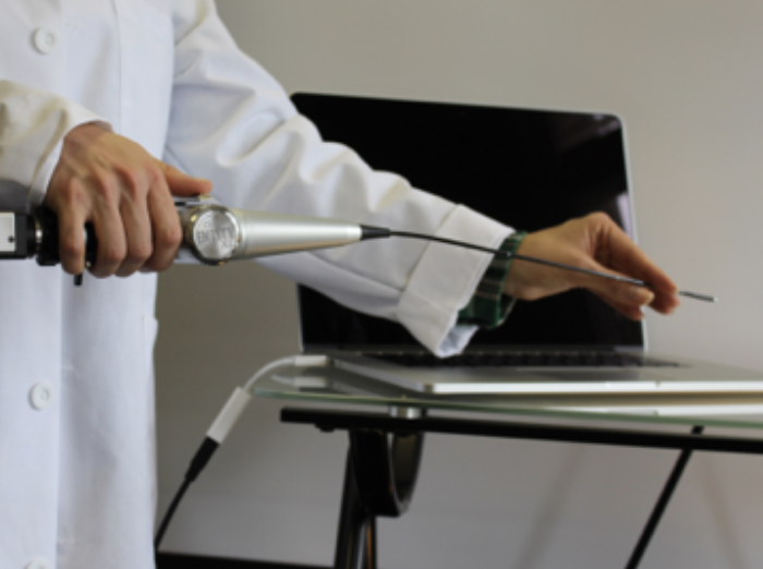 Medical specialist in a white lab coat holding a nasal endoscope attached to a laptop on a table.