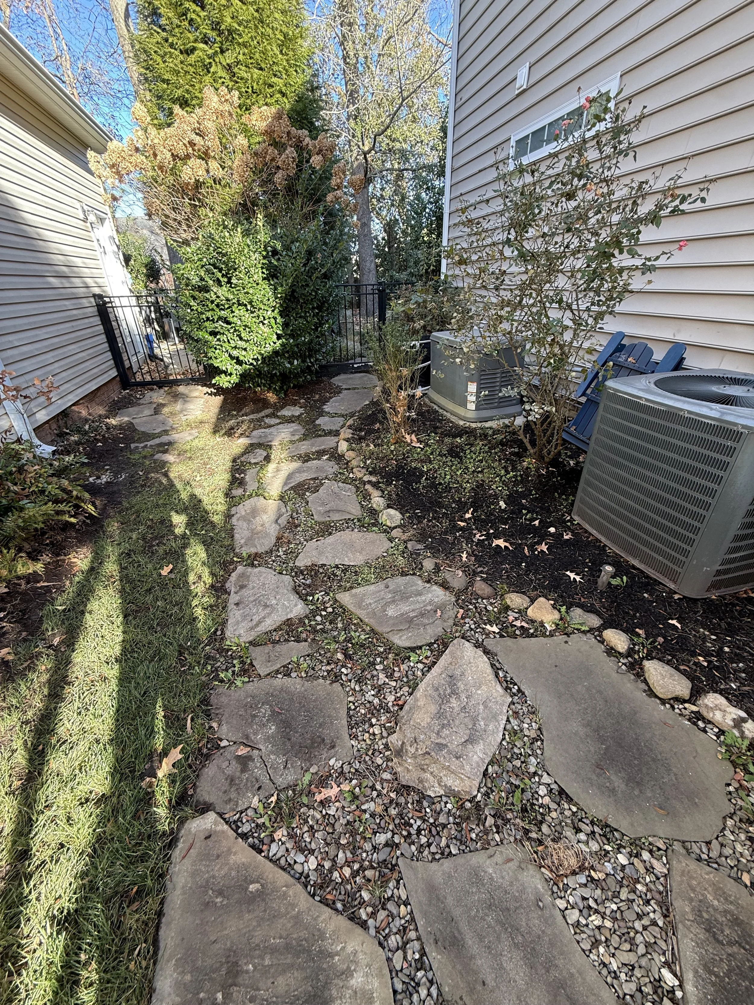 Backyard with stone pathway, plants, trees, and outdoor air conditioning units.