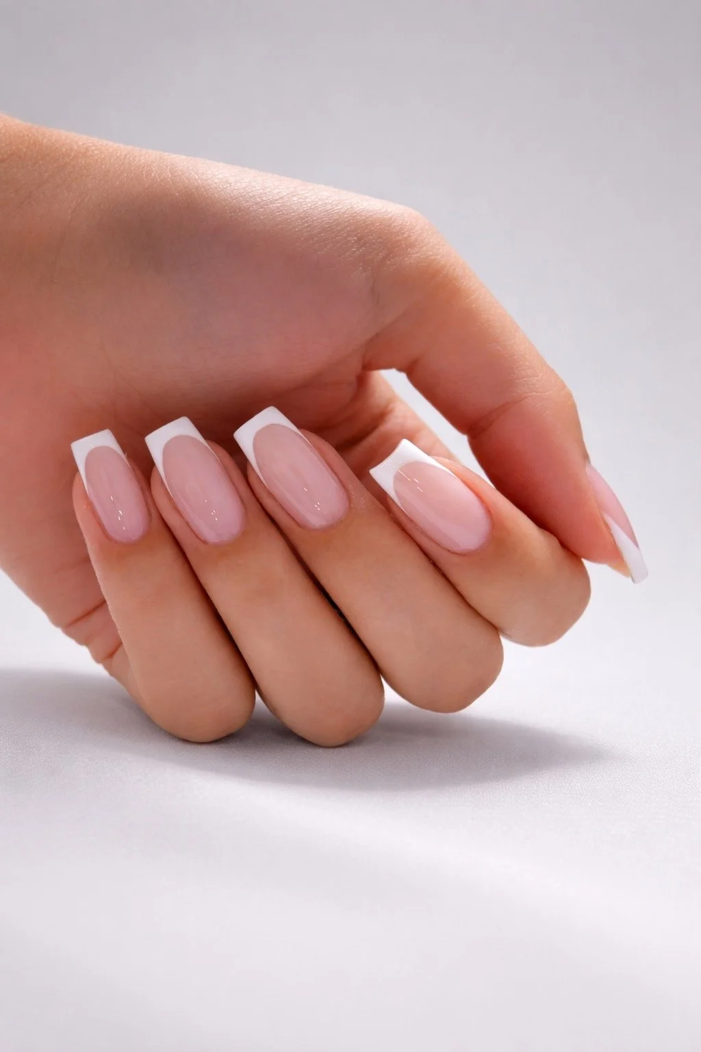 Close-up of a hand with manicured nails featuring a French manicure style, with natural pink base and white tips, resting on a white surface.
