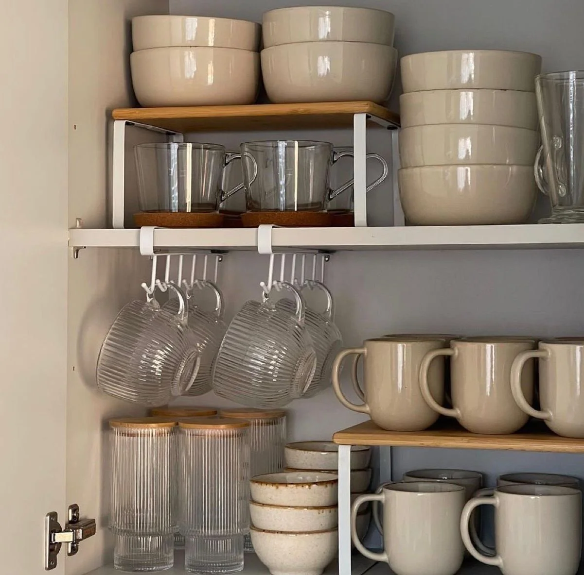 Kitchen cabinet shelf holding stacks of white bowls, glass mugs, and cups, with hanging glassware, and drinking glasses on the bottom.