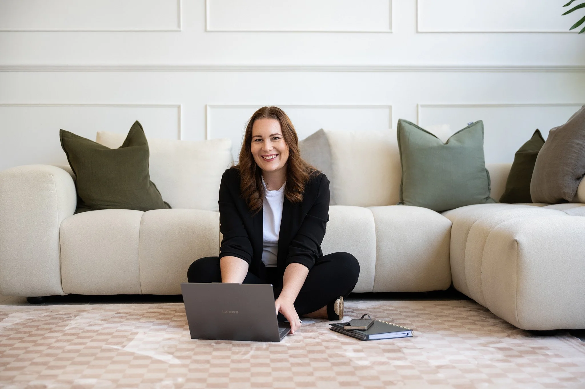 Tracey sitting on the ground in front of a couch working on her laptop and smiling