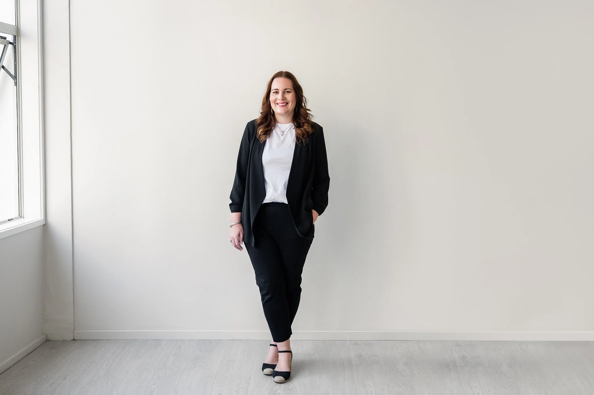 Tracey standing in a white studio setting, wearing a black blazer, pants and a white t-shirt