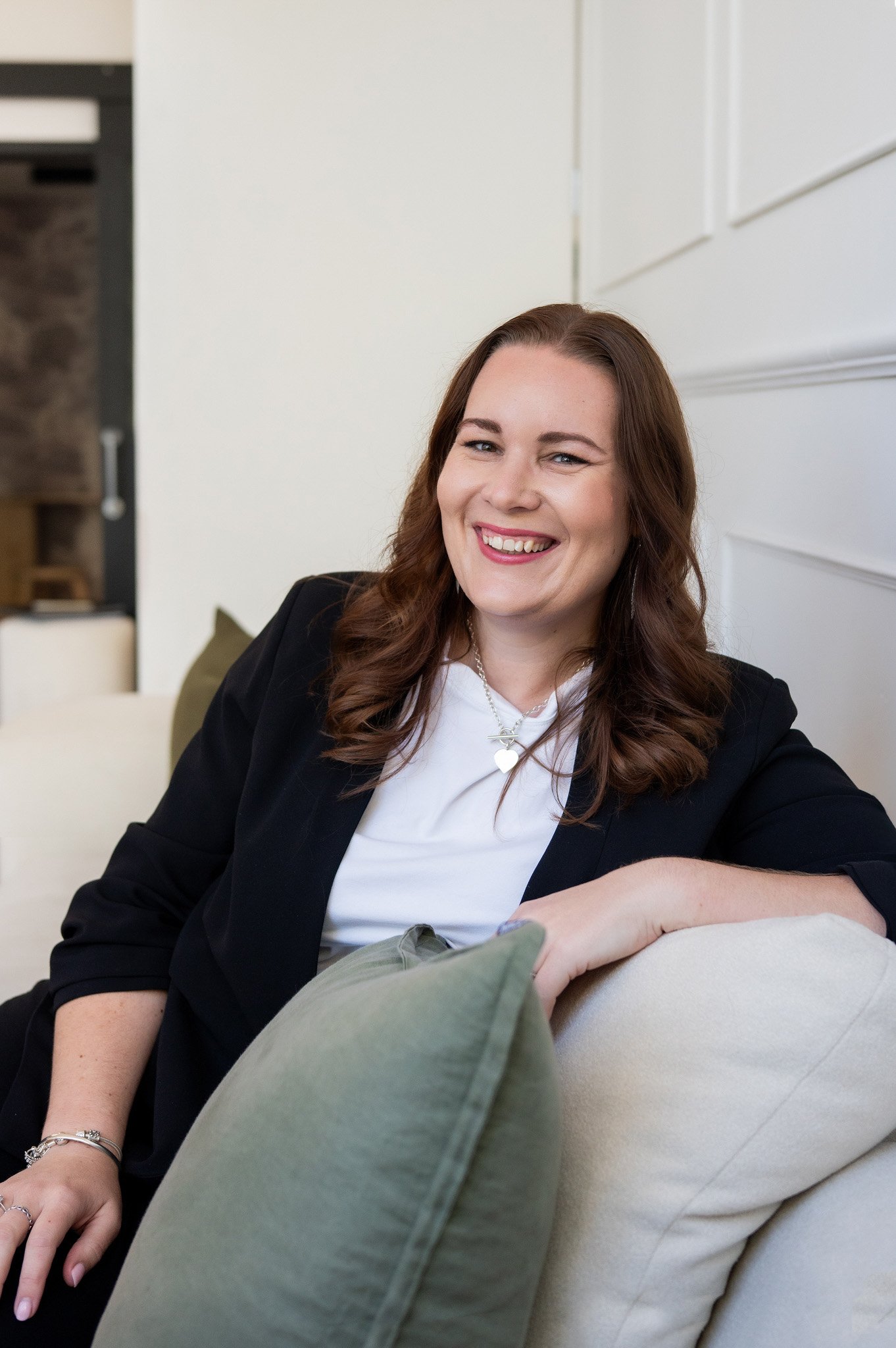 Tracey sitting on a couch, smiling and wearing a black blazer and white t-shirt