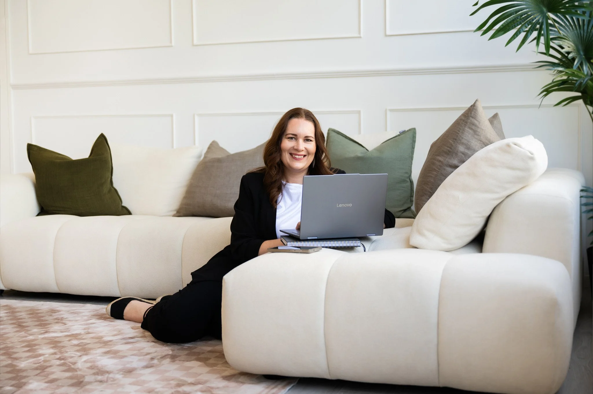 Tracey Lock sitting on the ground, working on her laptop that's sitting on the couch next to her