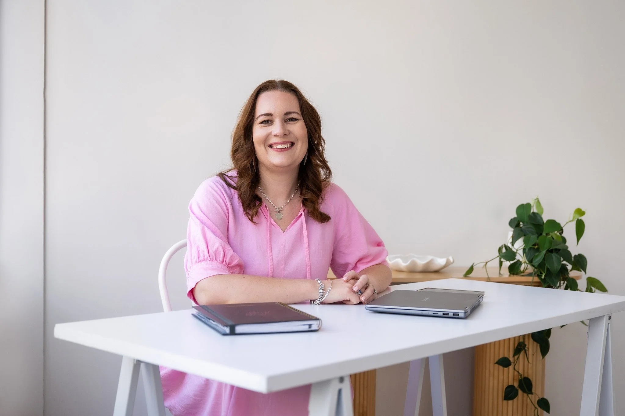 Tracey smiling at her desk, with her laptop and notebook