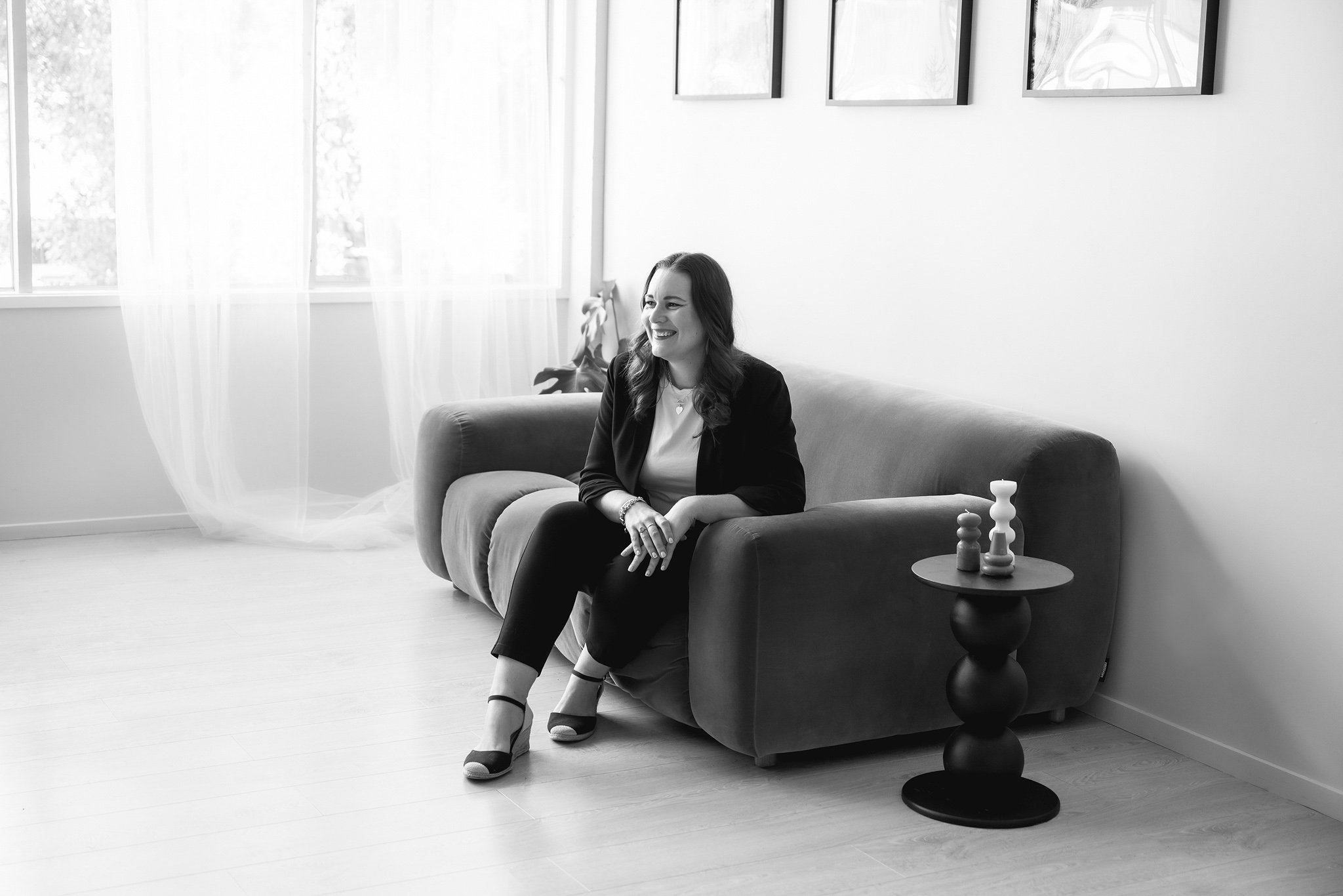 Black and white image of Tracey sitting on a couch casually and looking to the side while smiling