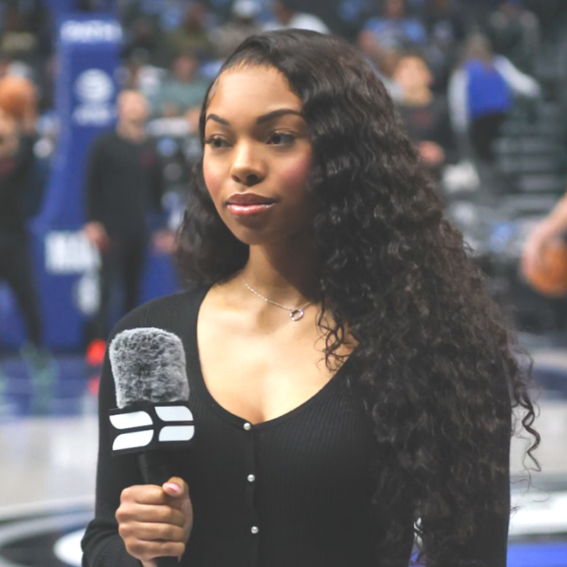 A young woman with long curly hair holding a microphone at a sports event or press conference.