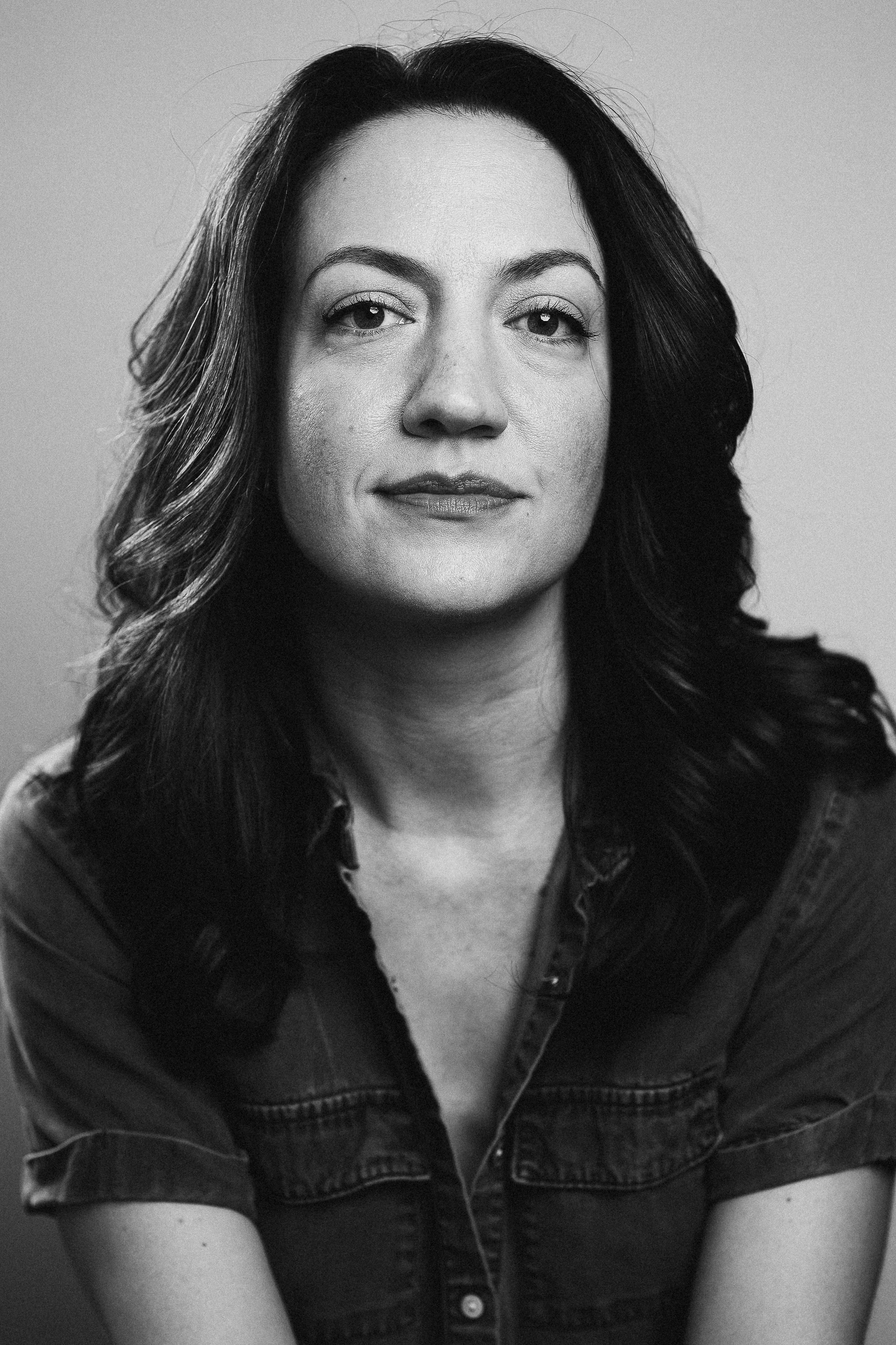 Black and white portrait of a woman with wavy hair, wearing a denim shirt, looking directly at the camera.