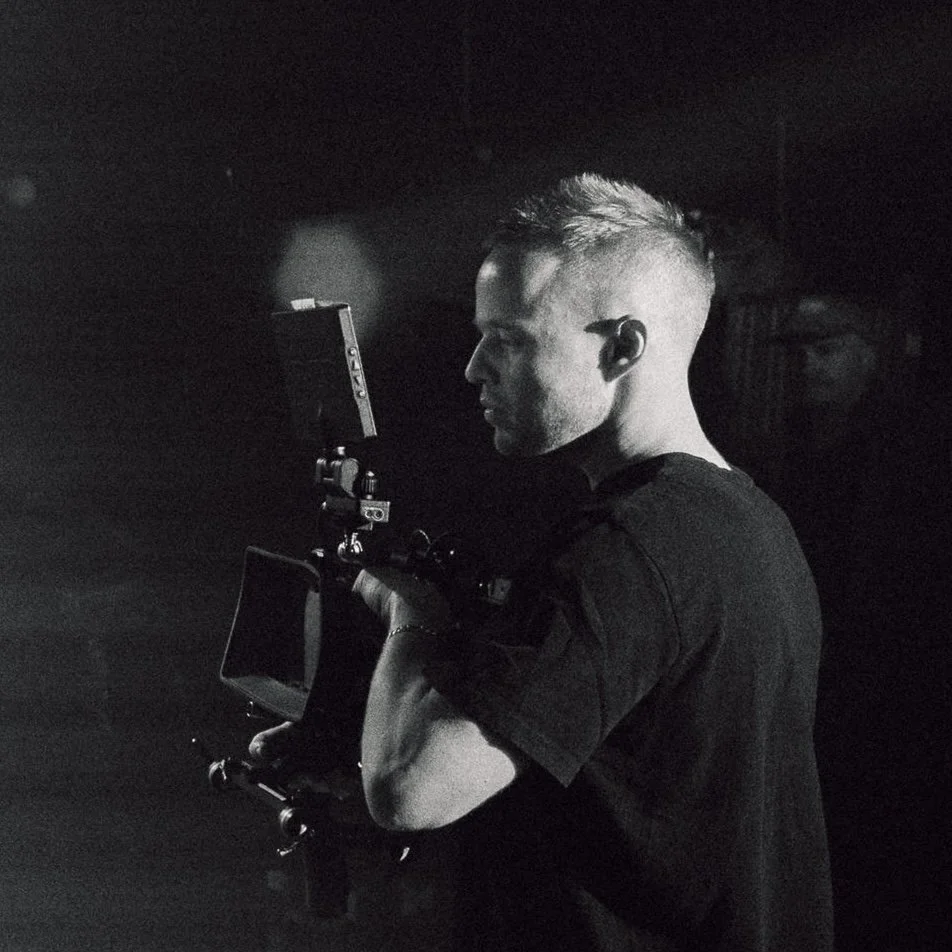 A man operating a professional camera with a monitor in a dark environment.