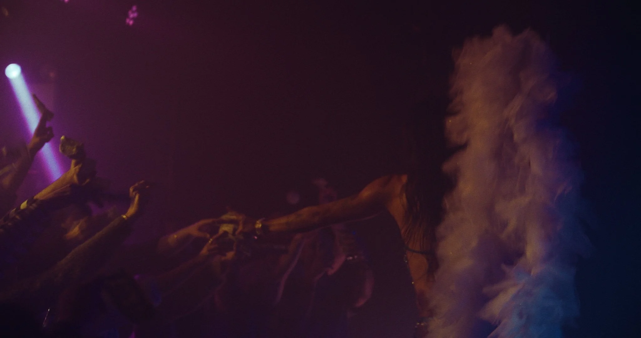 People dancing in a dark, smoky nightclub with purple lighting.
