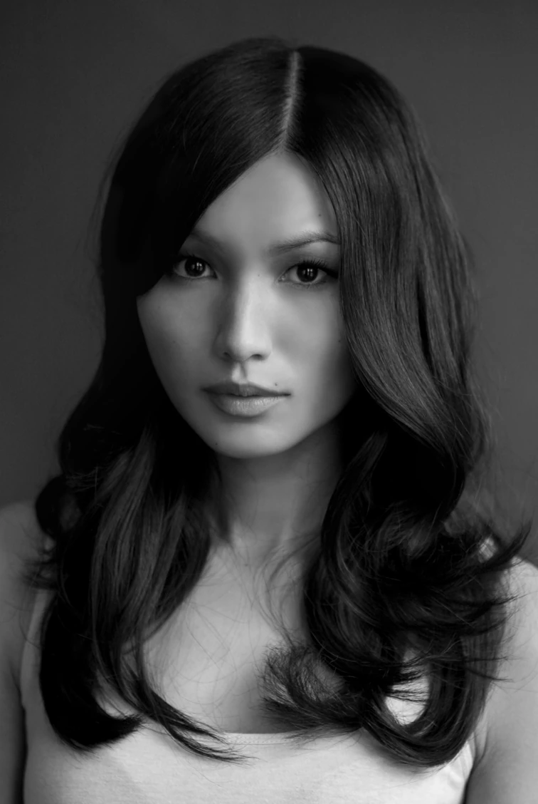 Black-and-white portrait of a woman with long wavy hair, looking directly at the camera with a neutral expression.