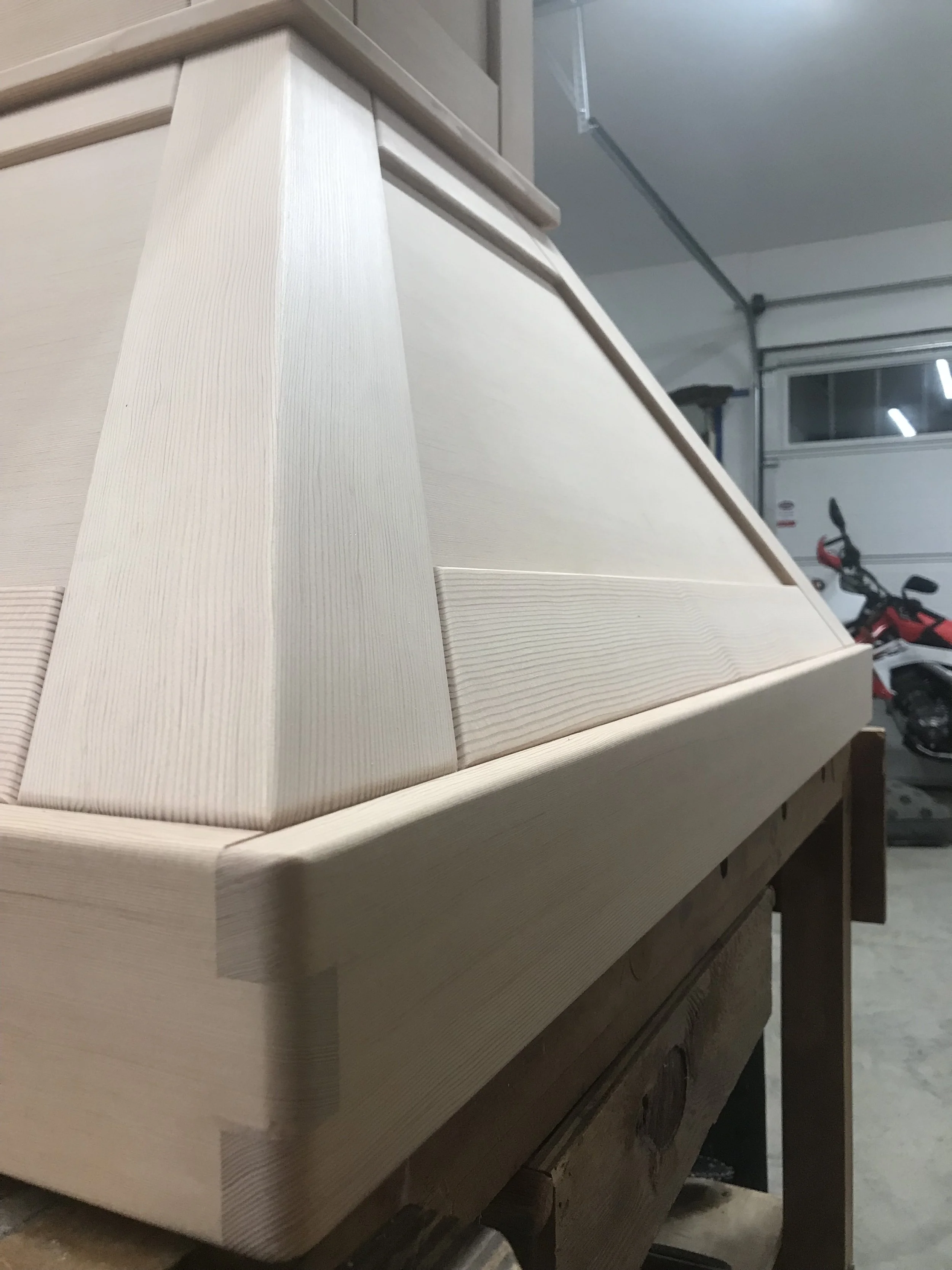 Ark Built Carpentry custom designed vent hood close up surrounded by tools and materials, including a workbench, power tools, and shelving.
