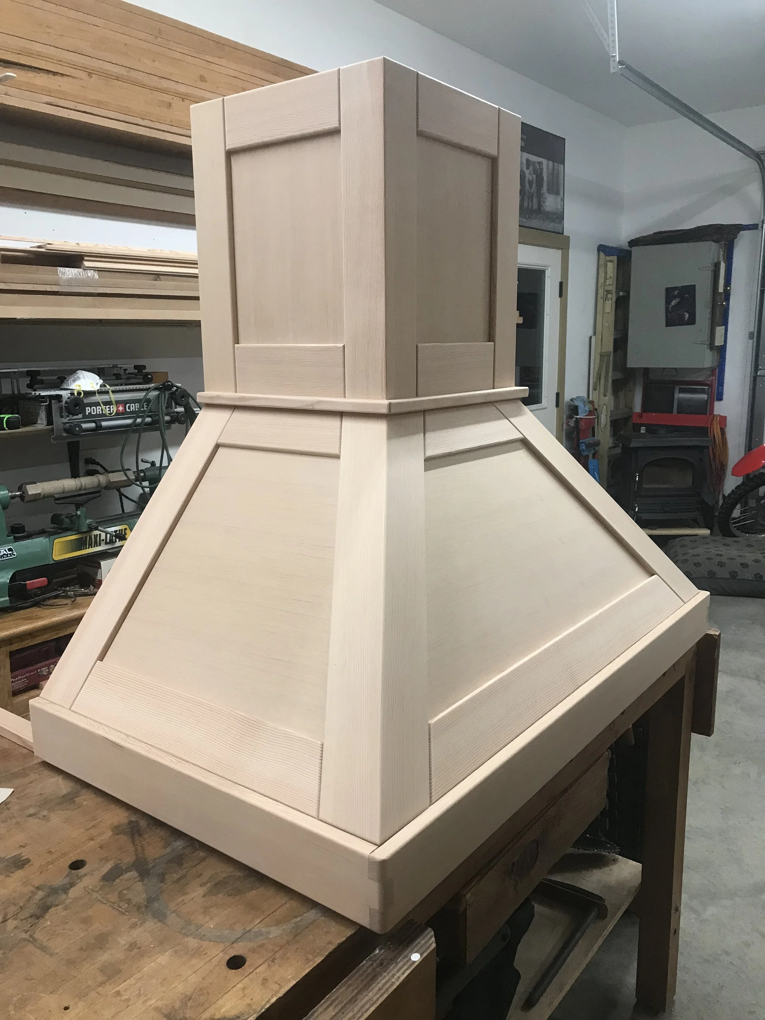 Ark Built Carpentry custom designed vent hood surrounded by tools and materials, including a workbench, power tools, and shelving.