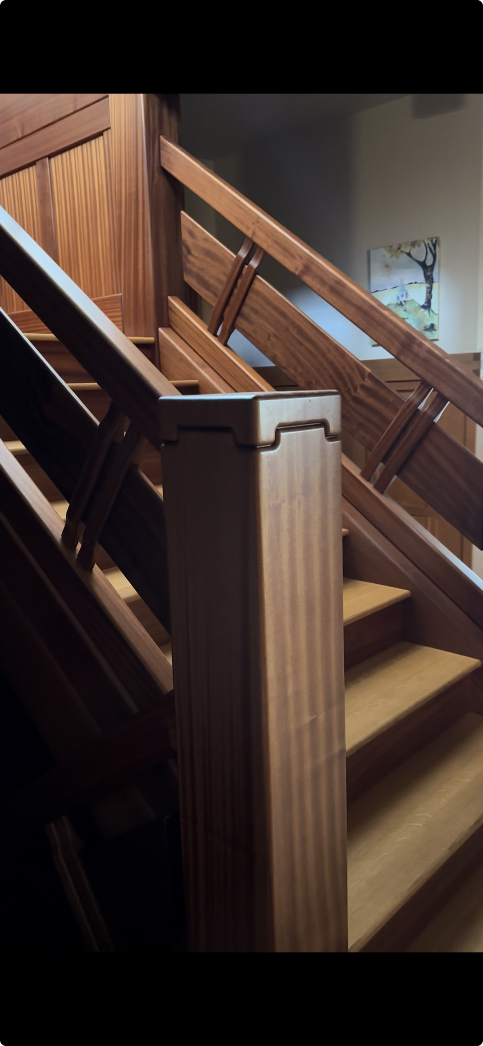 Ark Built Carpentry custom designed wooden staircase with a focus on the banister and handrails, featuring a custom handcrafted wood-paneled wall.